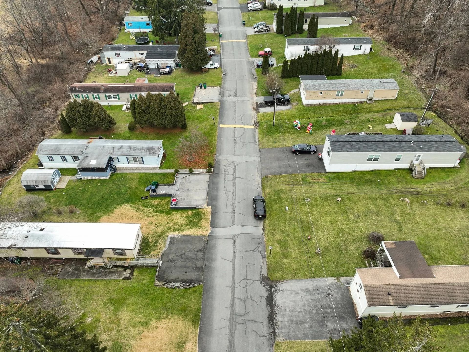 Aerial view of a quiet mobile home park with a central road, scattered trailers, and sparse trees.