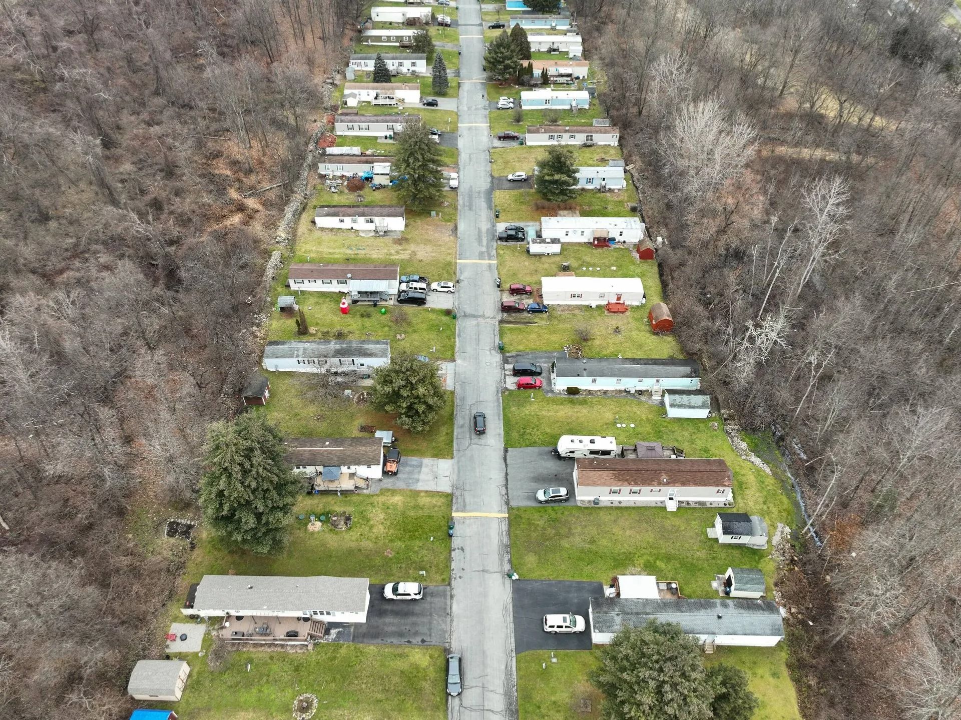 Aerial view of a narrow road through a wooded mobile home park with trailers on both sides.