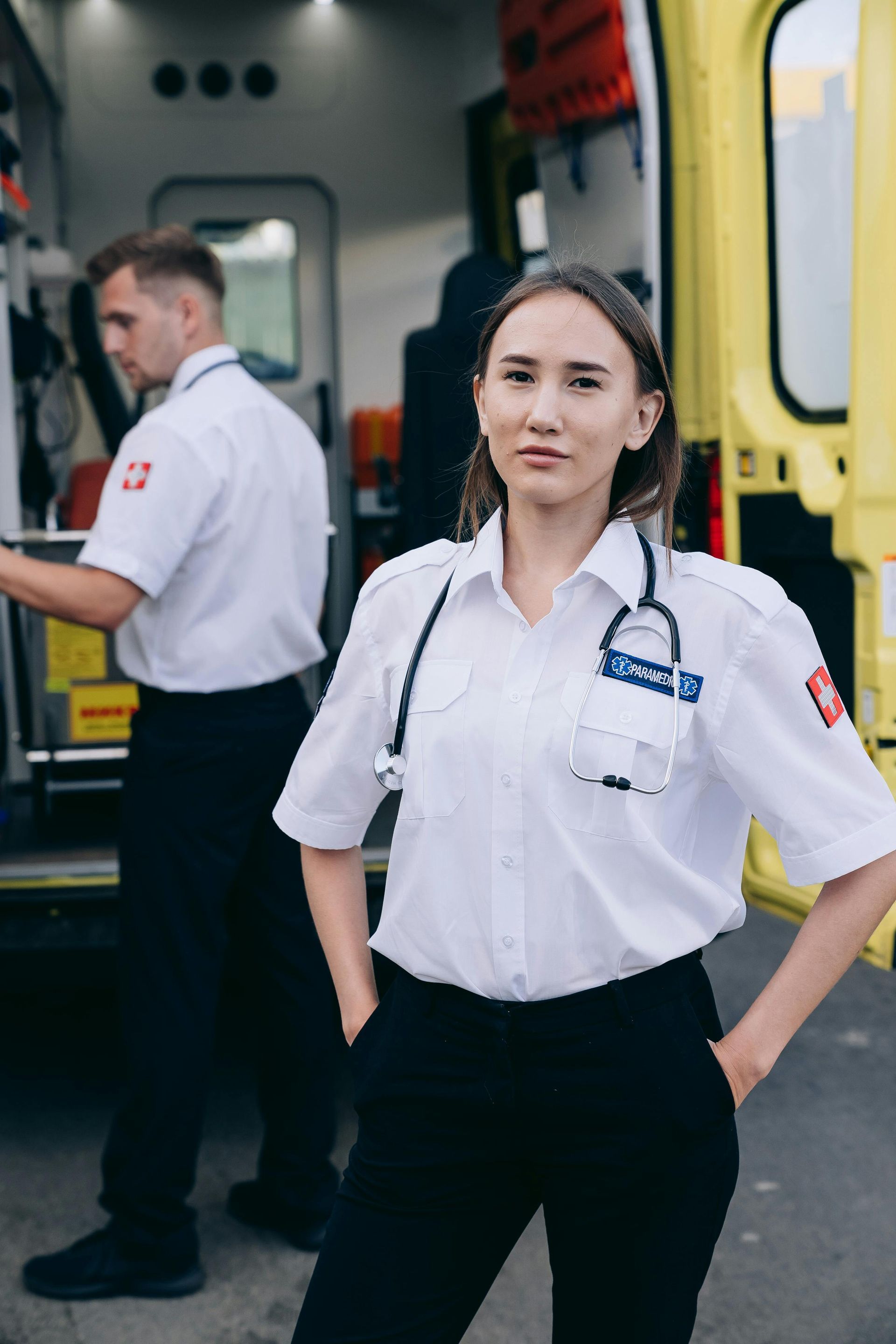 Paramedic standing beside an ambulance, wearing a white shirt and black pants.