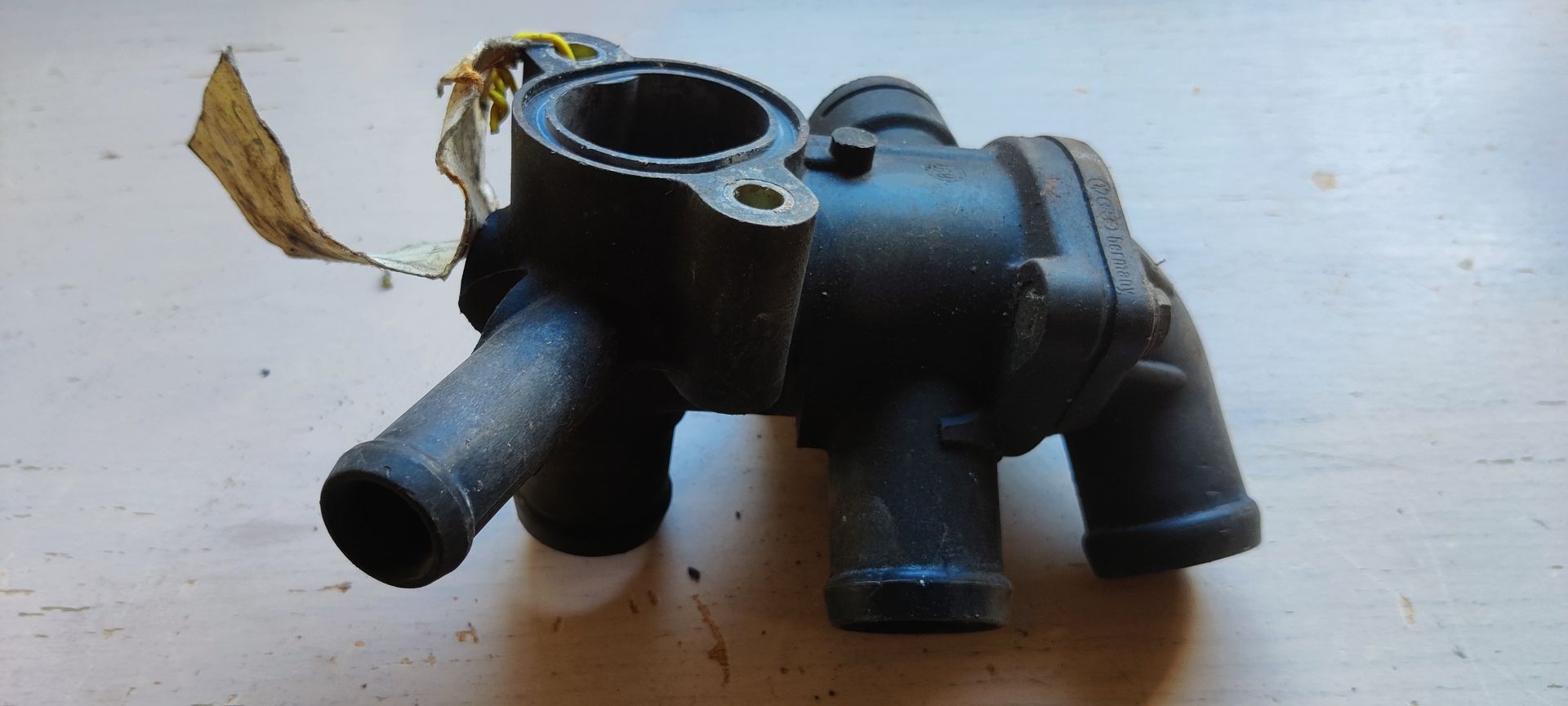 Een zwarte kunststof thermostaatbehuizing voor de koelvloeistof van een automotor, met meerdere aansluitpunten voor slangen.