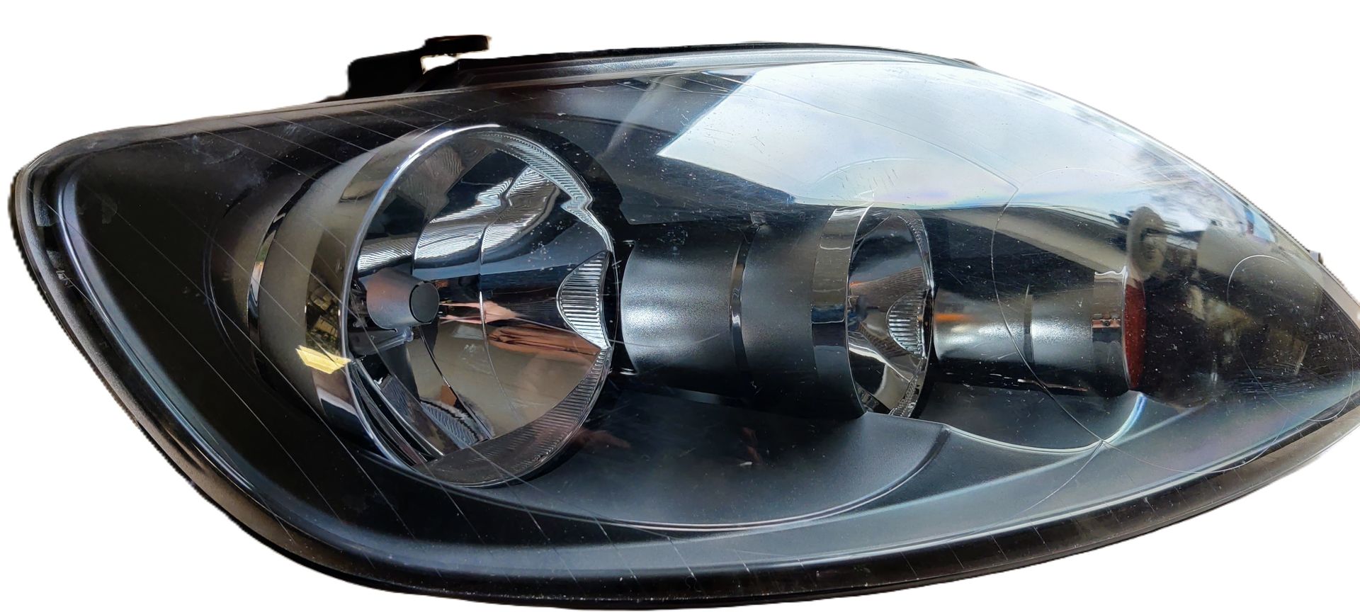Een zwarte autokoplampunit met transparante lenzen en twee ronde reflectoren, geïsoleerd tegen een witte achtergrond.