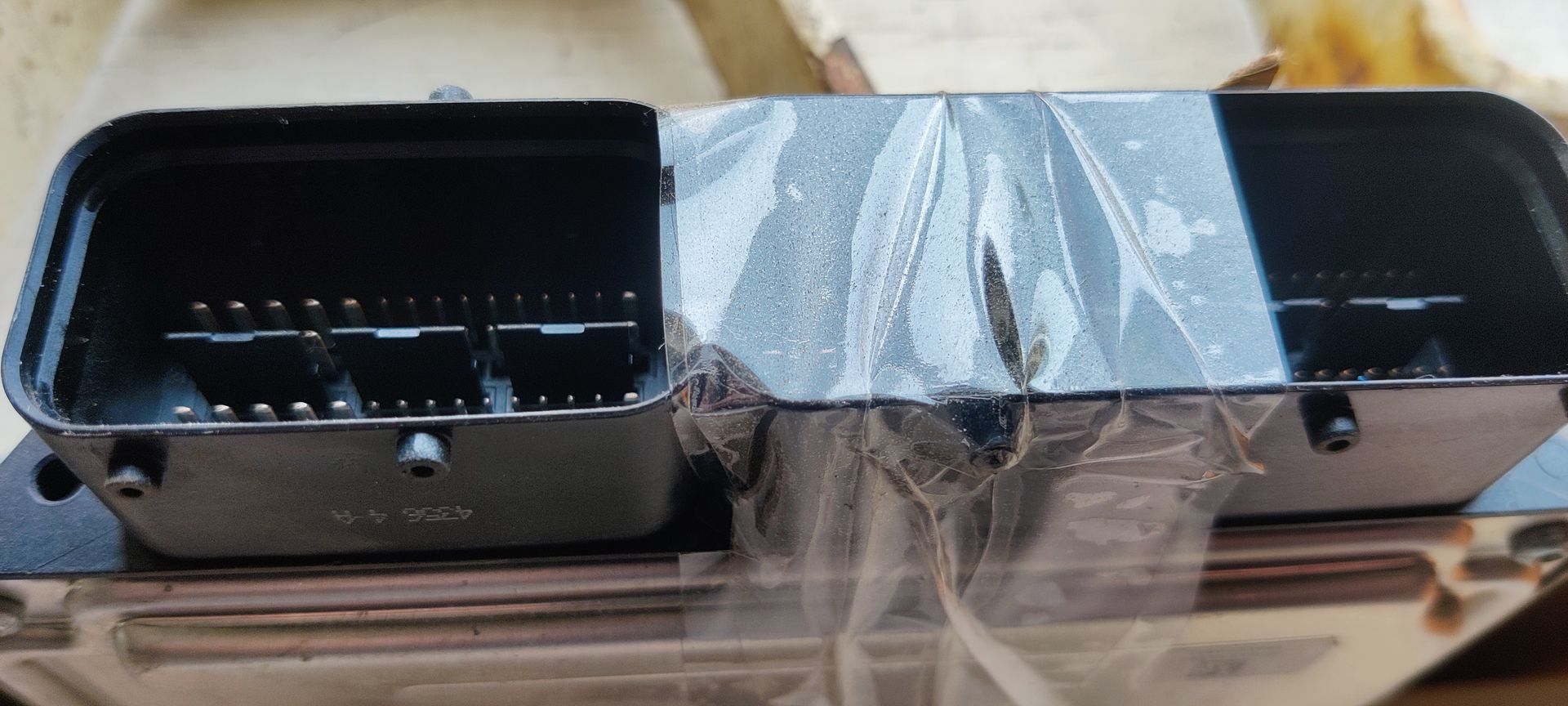 Een grijze ECU (Engine Control Unit) van een auto met een handgeschreven geel identificatielabel, op een witte achtergrond.