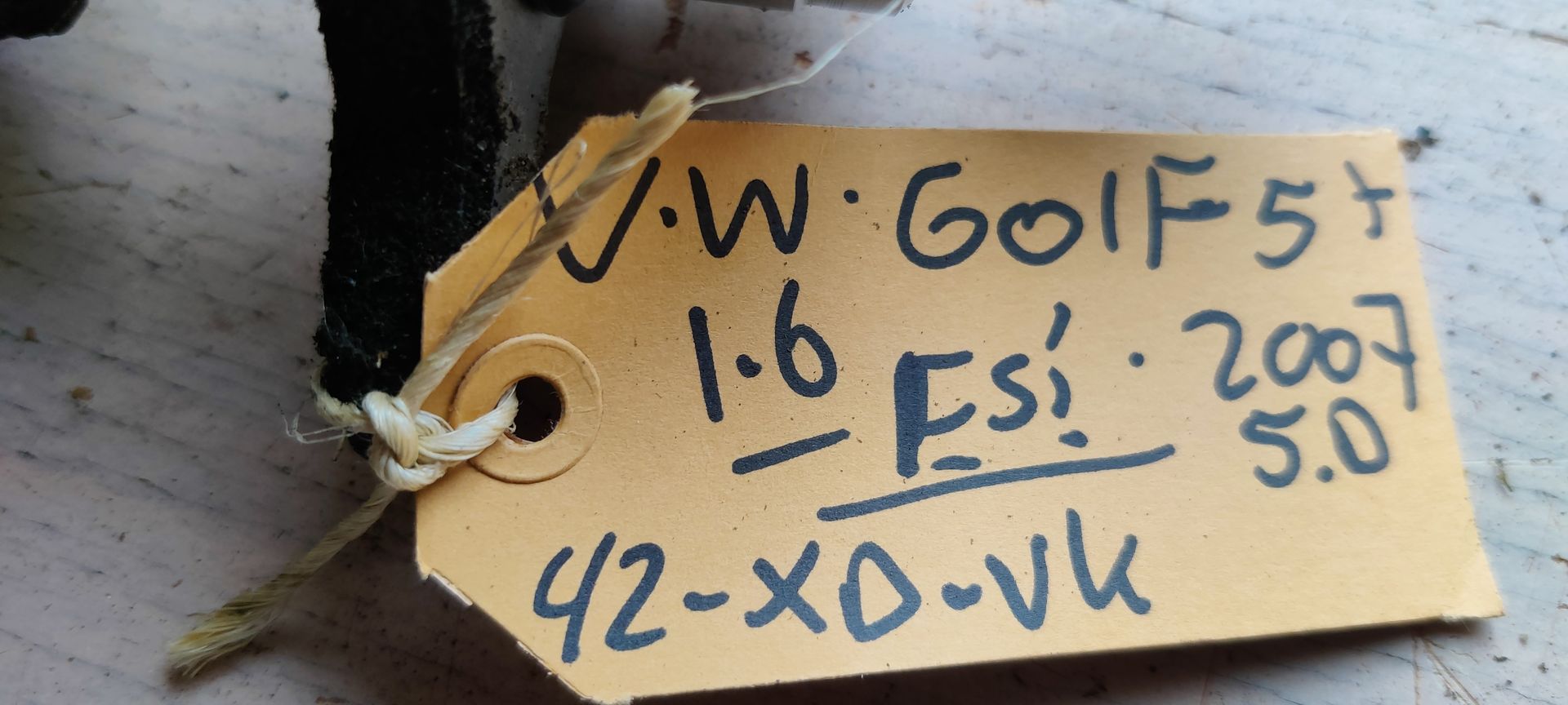 Een hoofdremcilinder van een auto met een doorschijnend plastic vloeistofreservoir en een klein identificatielabeltje.