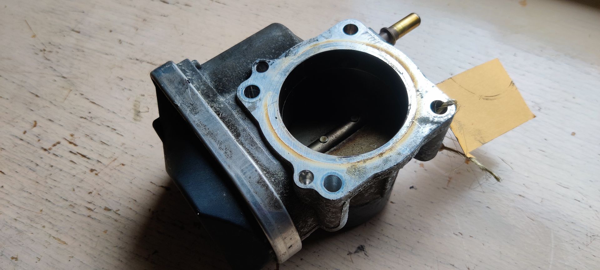 Een metalen gasklephuis voor auto's met een geïntegreerde zwarte elektronische actuator op een witte achtergrond.