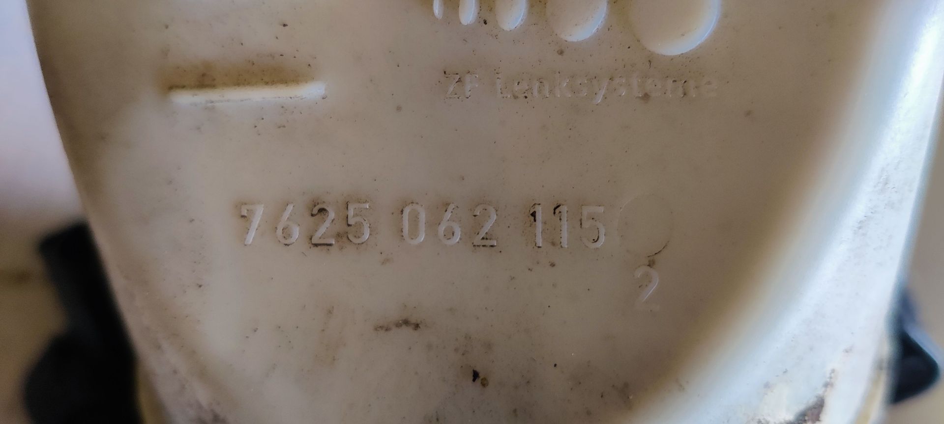 Een grijze elektrische stuurbekrachtigingsmotor voor auto's met een doorschijnend plastic reservoir en een barcode-sticker.