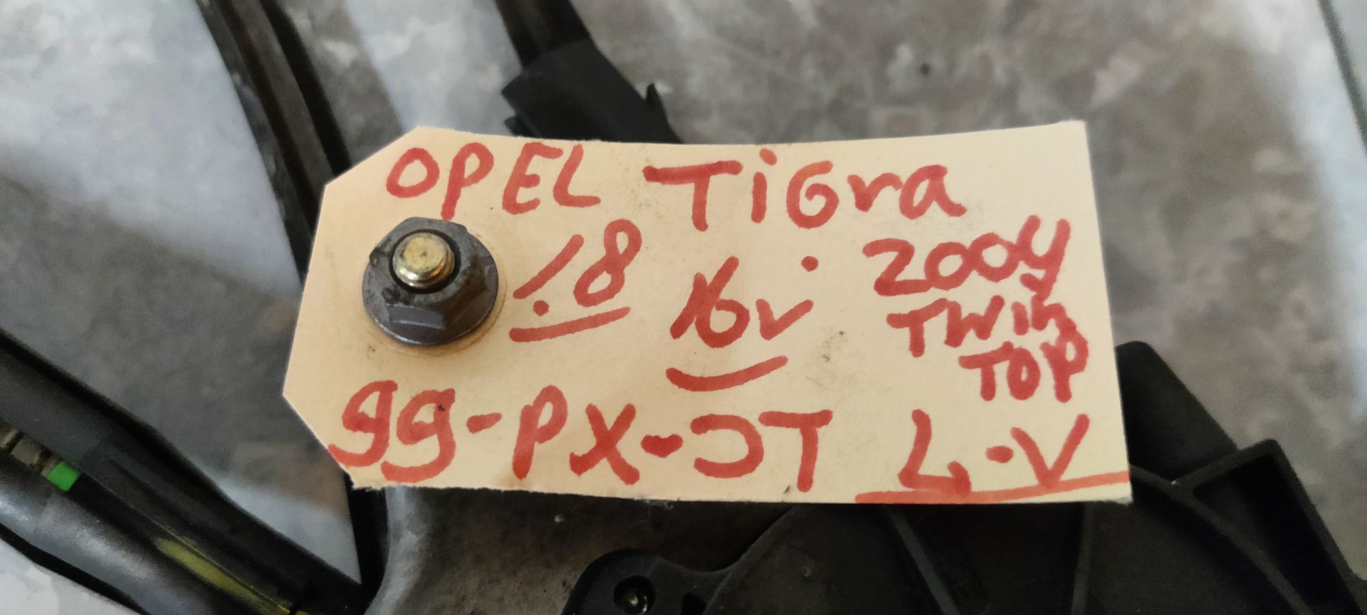Een metalen raammechanisme voor auto's met een zwarte motor en kabels, geplaatst op een grijze betonnen ondergrond.