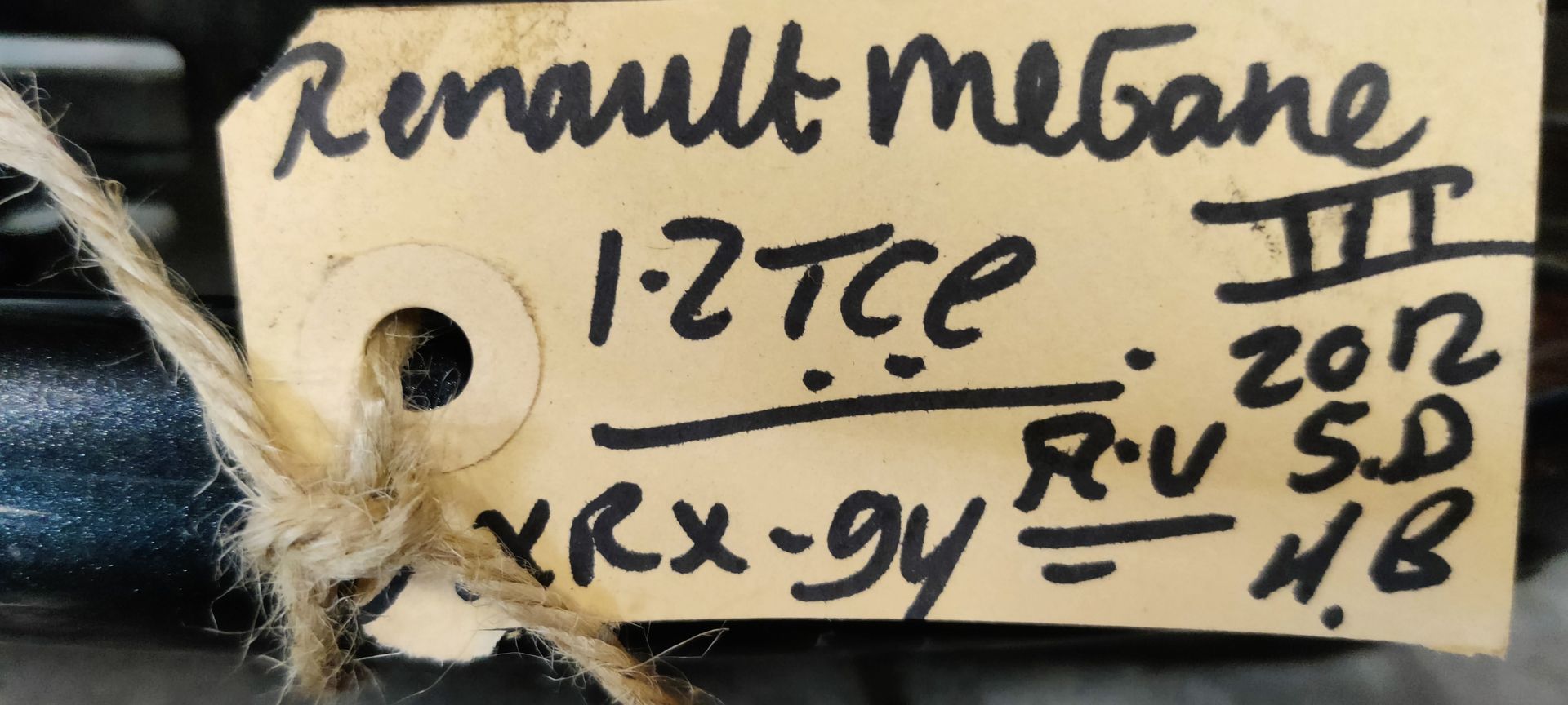 Een zwarte deurgreep voor een Renault Megane III met een handgeschreven identificatielabel, bevestigd met een touwtje.