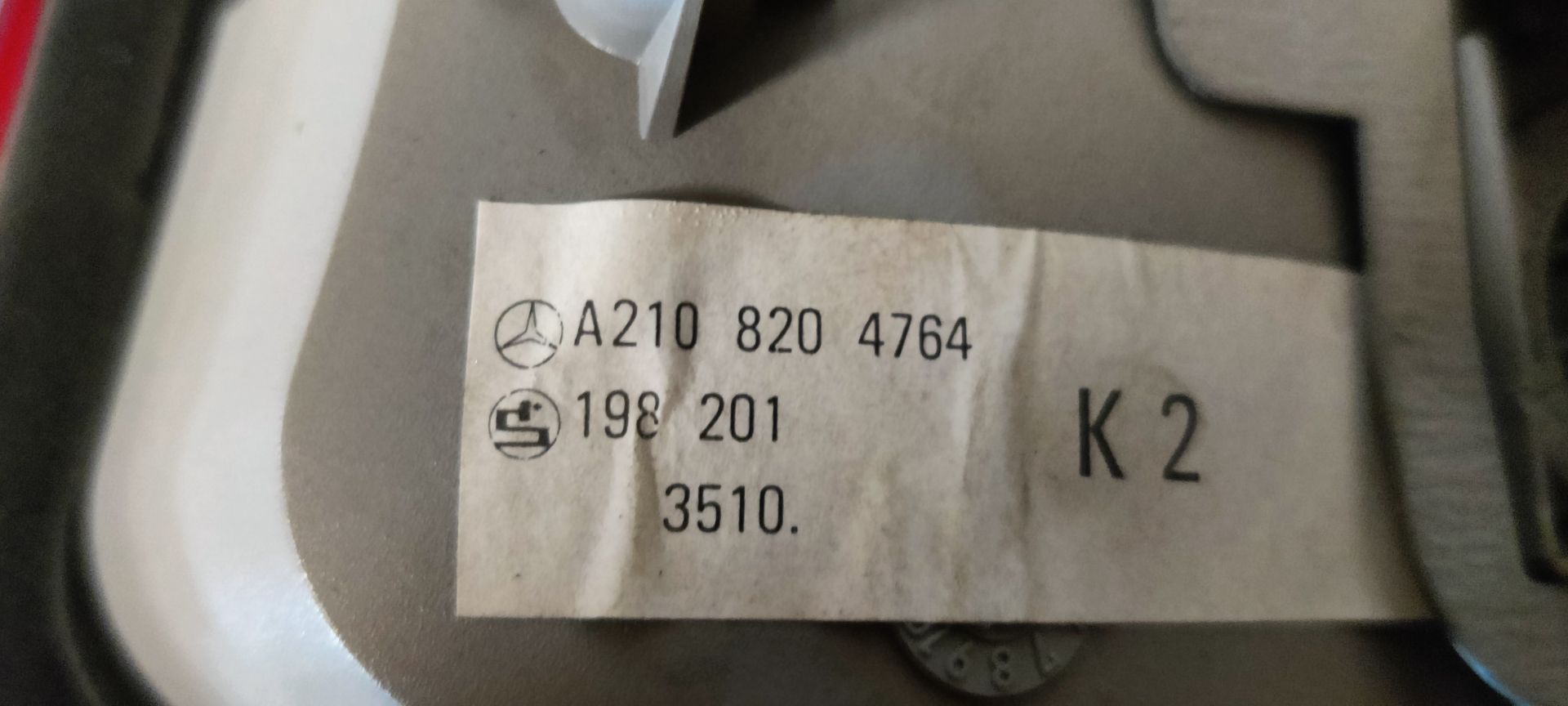 Een rode en transparante achterlichtunit van een auto, van voren gezien tegen een grijze, gestructureerde achtergrond.