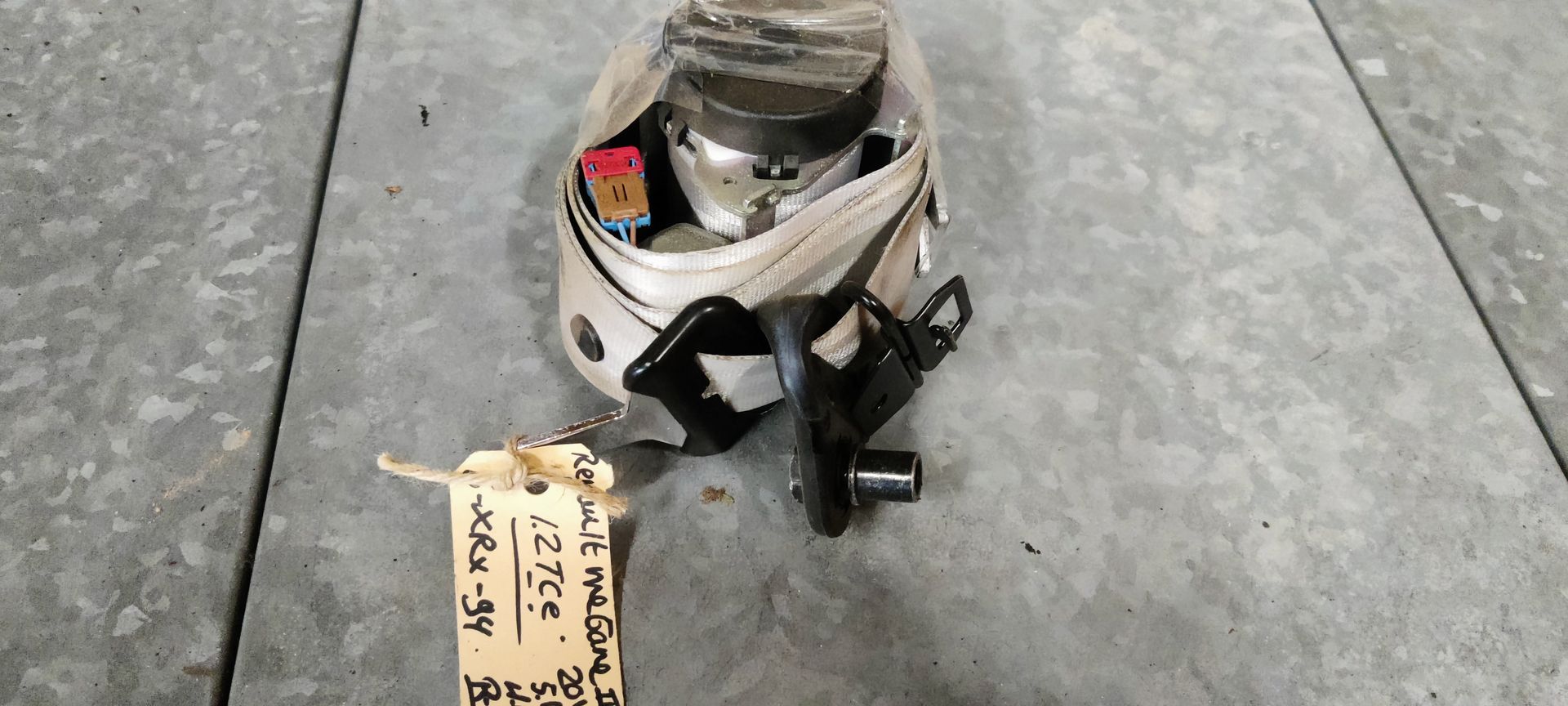 Een oprolmechanisme voor een autogordel, inclusief de gordelband en een identificatielabel, op een grijze ondergrond.