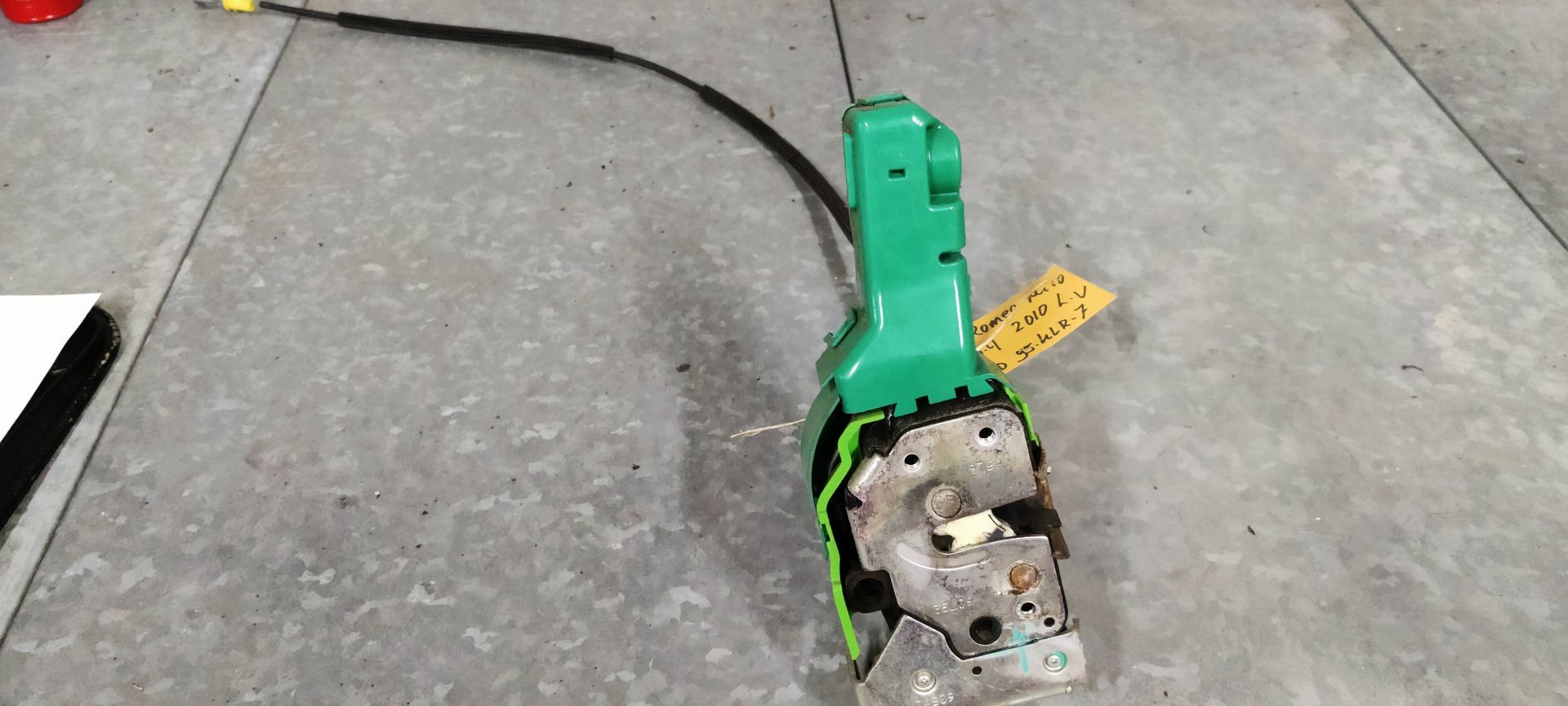 Een groen autodeurslot met kabel eraan, liggend op een grijze betonnen vloer.