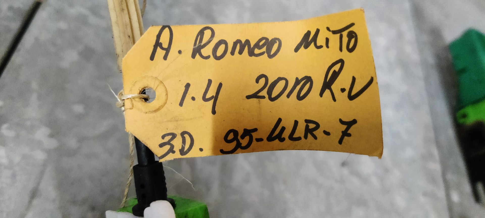 Een groen autodeurslotmechanisme met een aangesloten kabel, dat op een grijze tegelvloer ligt.