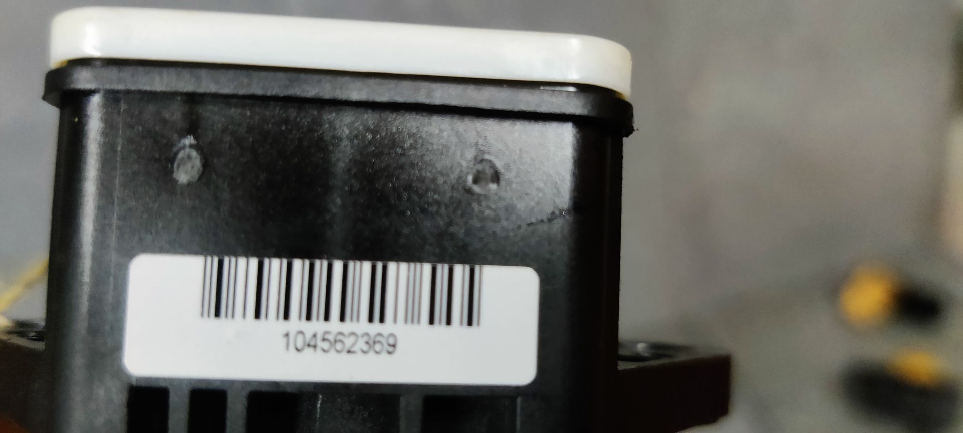 Een zwart-witte Bosch auto-elektronicaregeleenheid ligt op een grijs oppervlak met een geel label eraan.