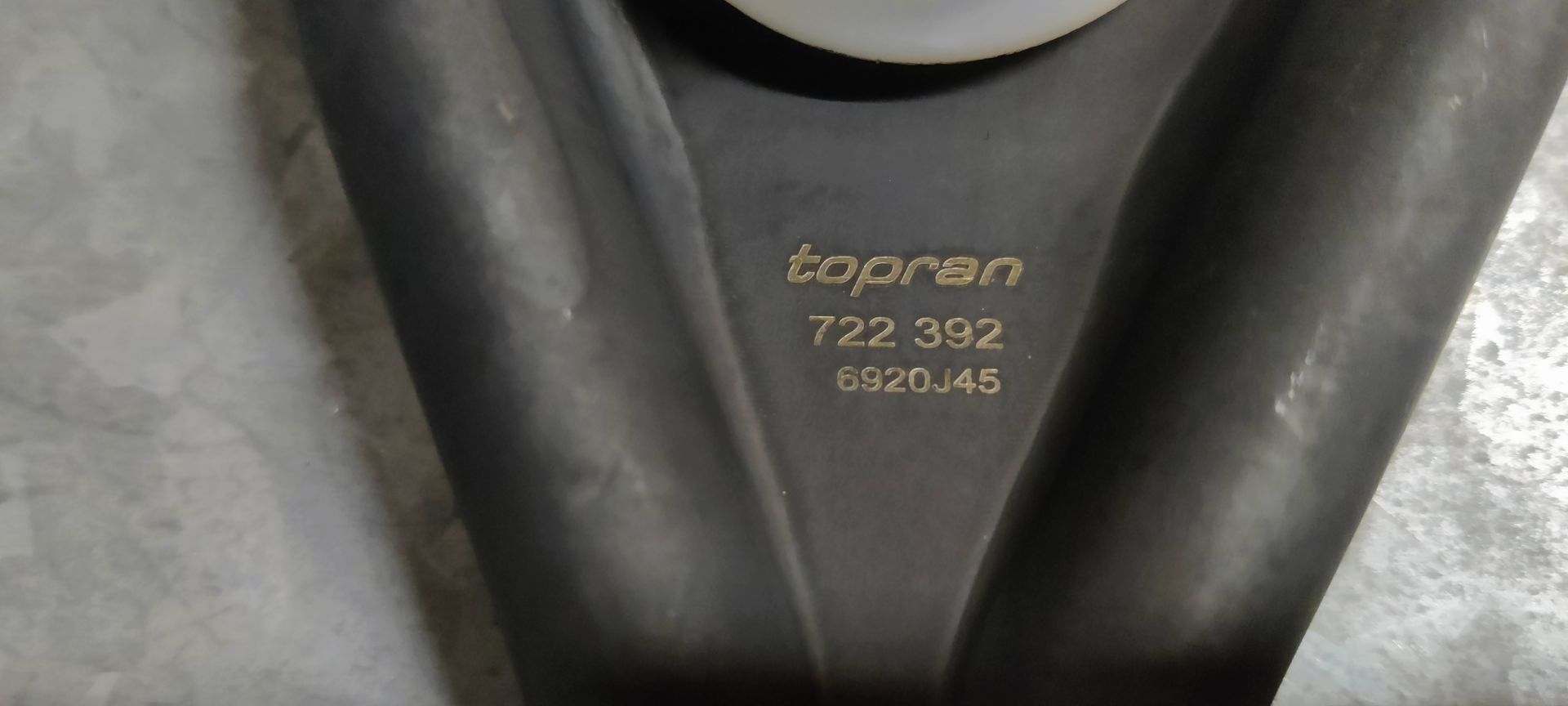 Een zwarte, Y-vormige koppelingsvork voor auto's met een witte plastic kogellagerbus, rustend op een betonnen ondergrond.