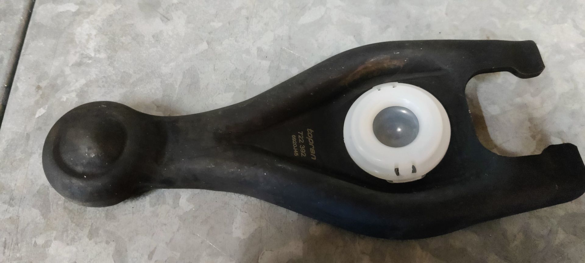 Een zwarte metalen koppelingsvork met een witte plastic kogellagerbus die op een lichtgekleurde ondergrond rust.