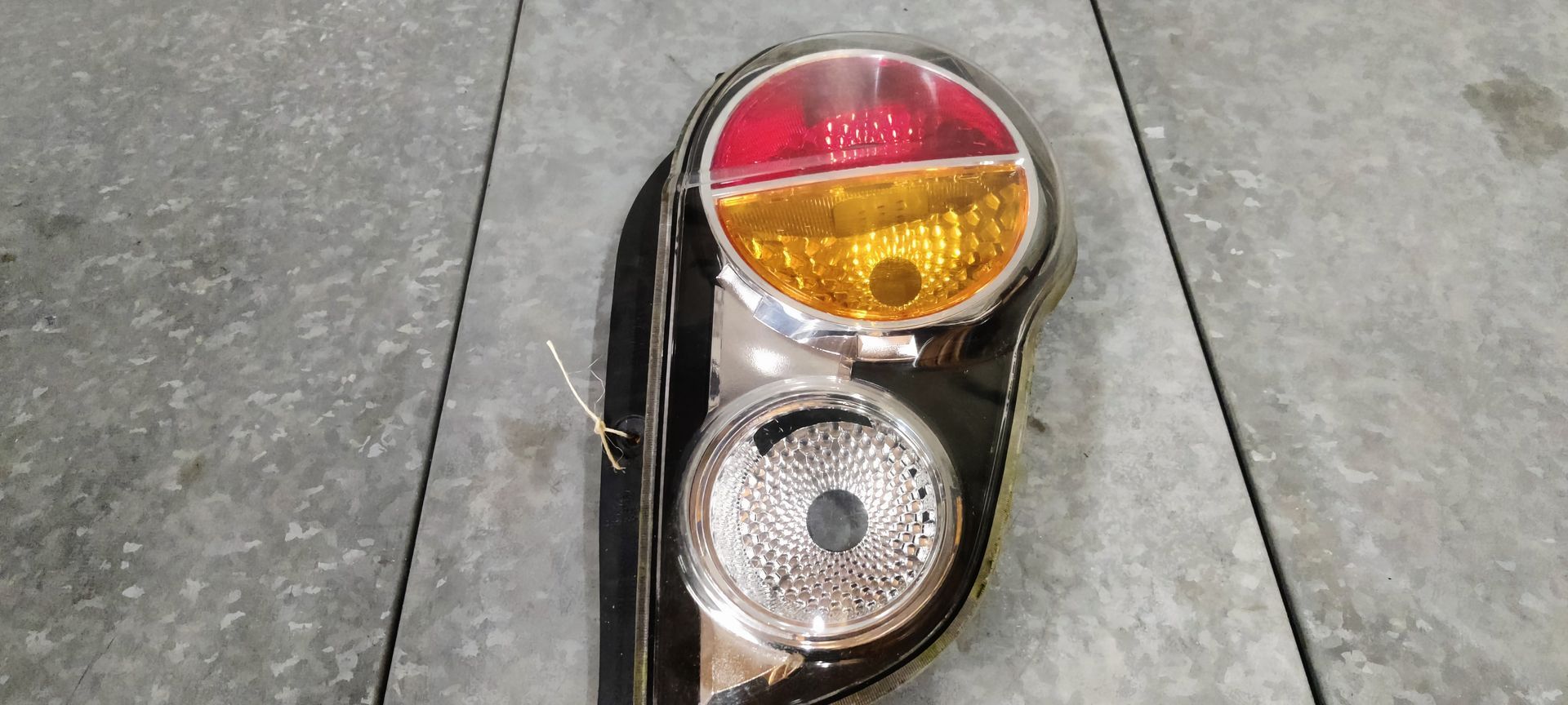 Een achterlichtunit van een auto op een grijze vloer, met rode, gele en transparante ronde lichtsegmenten.