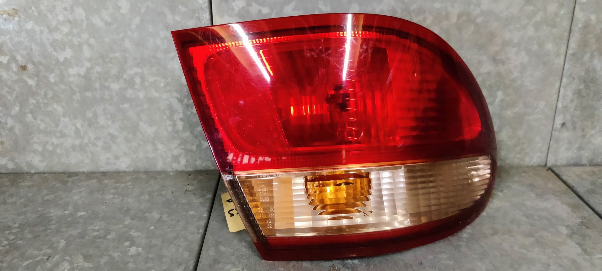 Een rode en amberkleurige achterlichtunit van een auto, geplaatst op een lichtgekleurde ondergrond.