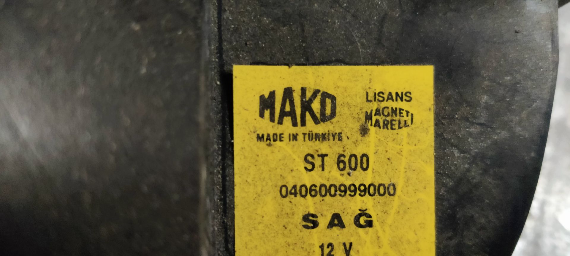 Een rode en transparante autoachterlichtunit met een klein labeltje eraan, rustend op een grijs metalen oppervlak.