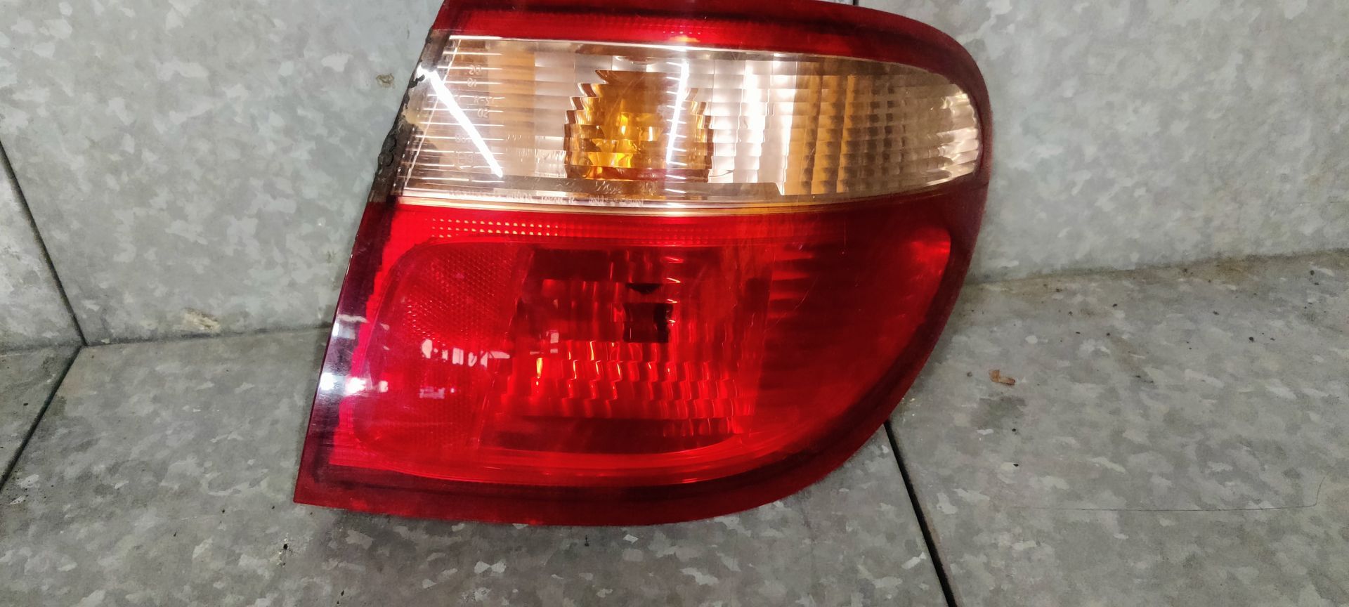 Een rode en transparante achterlichtunit van een auto, afgebeeld tegen een grijze, gestructureerde achtergrond.