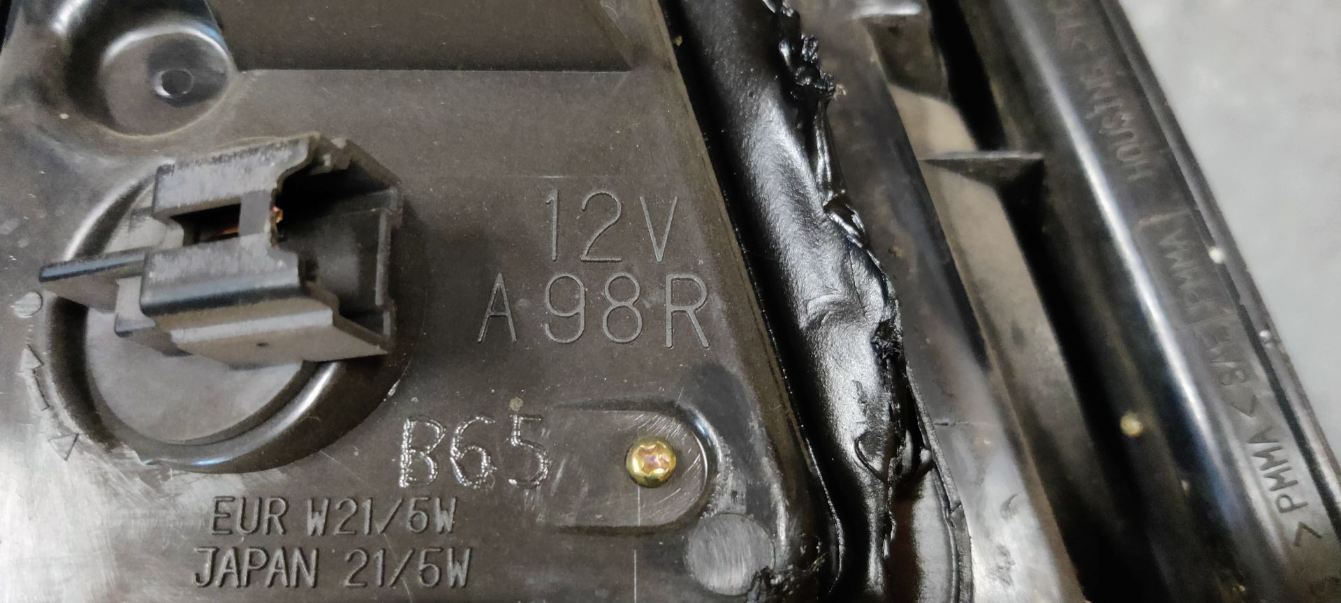 Een rode en transparante achterlichtunit van een auto, afgebeeld tegen een grijze, gestructureerde achtergrond.