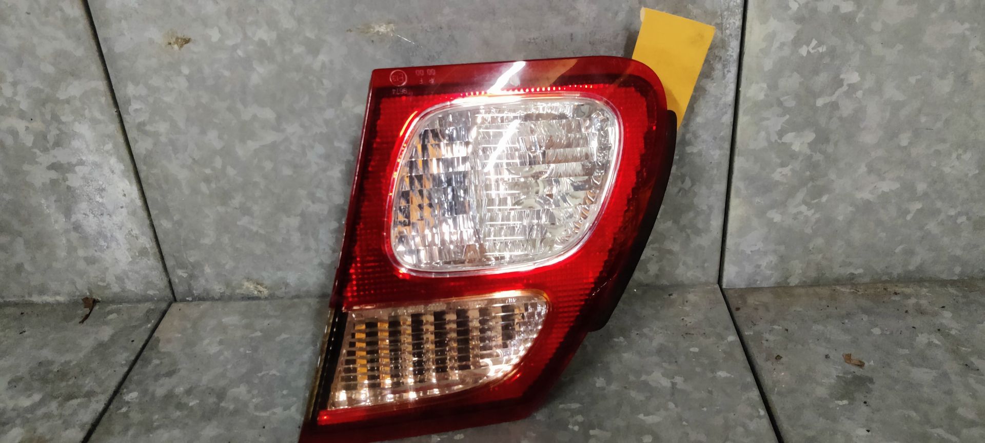 Een rode en transparante plastic achterlichtunit voor auto's, geïsoleerd tegen een lichtgrijze metallic achtergrond.
