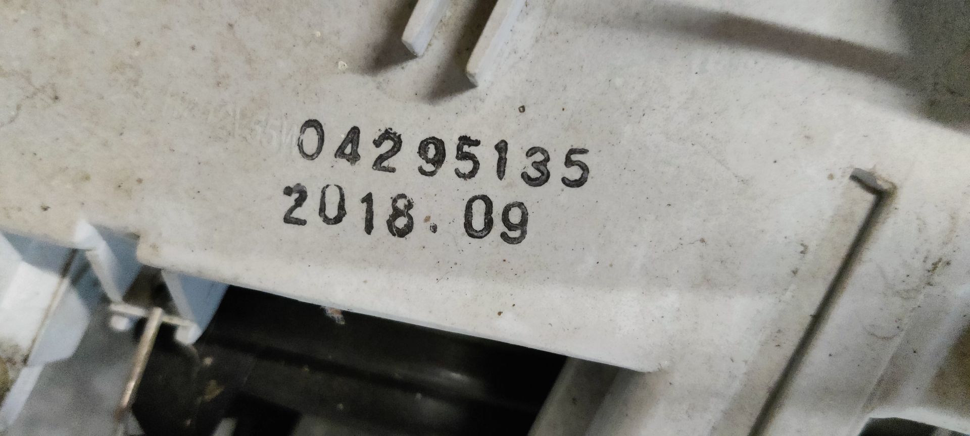 Een autokoplampunit met helder glas, verchroomde binnenreflectoren en een aangehecht identificatielabel.