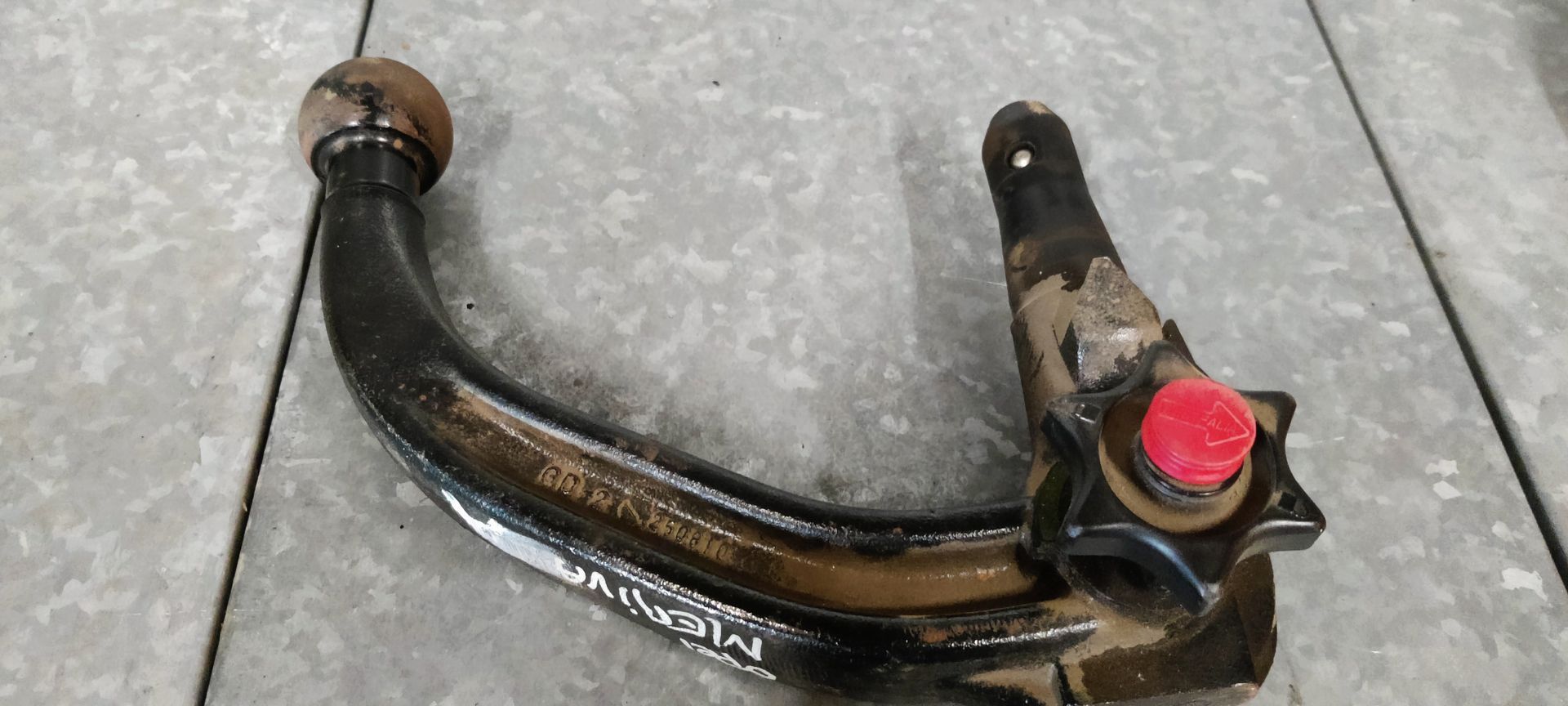 Een afneembare trekhaak met een zwarte gebogen arm, een stervormige vergrendelingsknop en een rode knop in het midden.