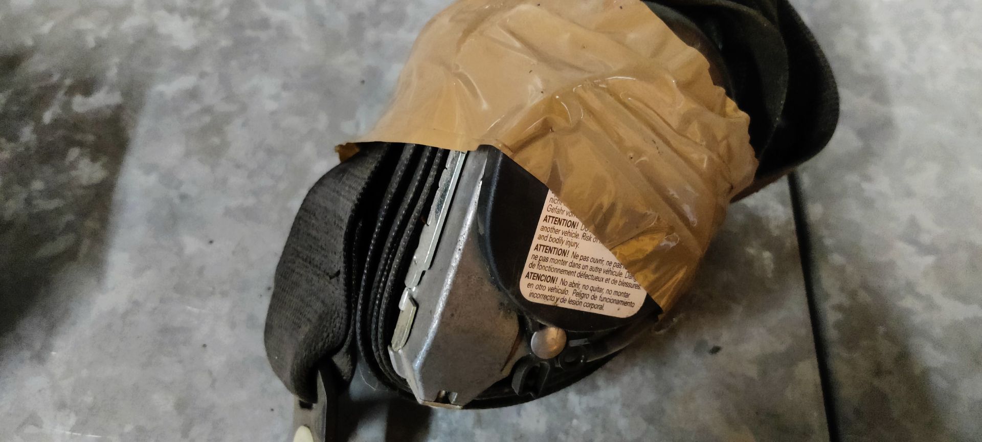 Een opgerolde zwarte veiligheidsgordel, vastgeplakt met beige verpakkingstape, en een handgeschreven waarschuwingsbriefje.