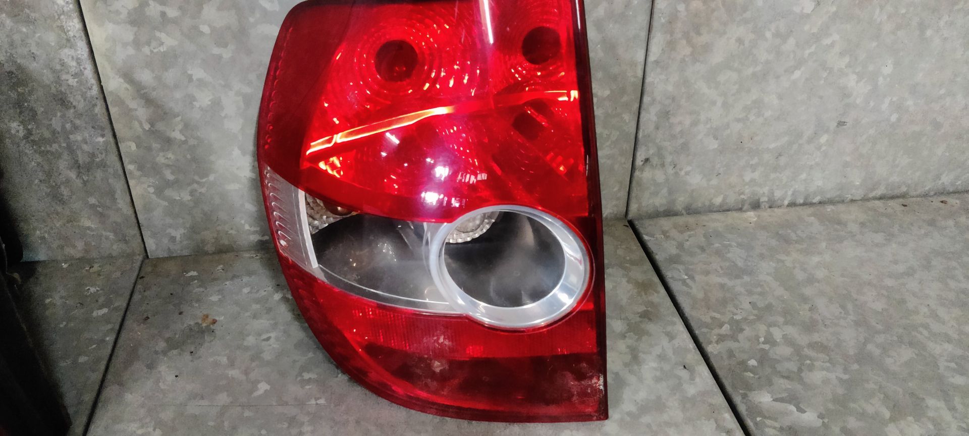 Een rode en transparante achterlichtunit van een auto, recht van voren gezien tegen een grijze tegelwand.