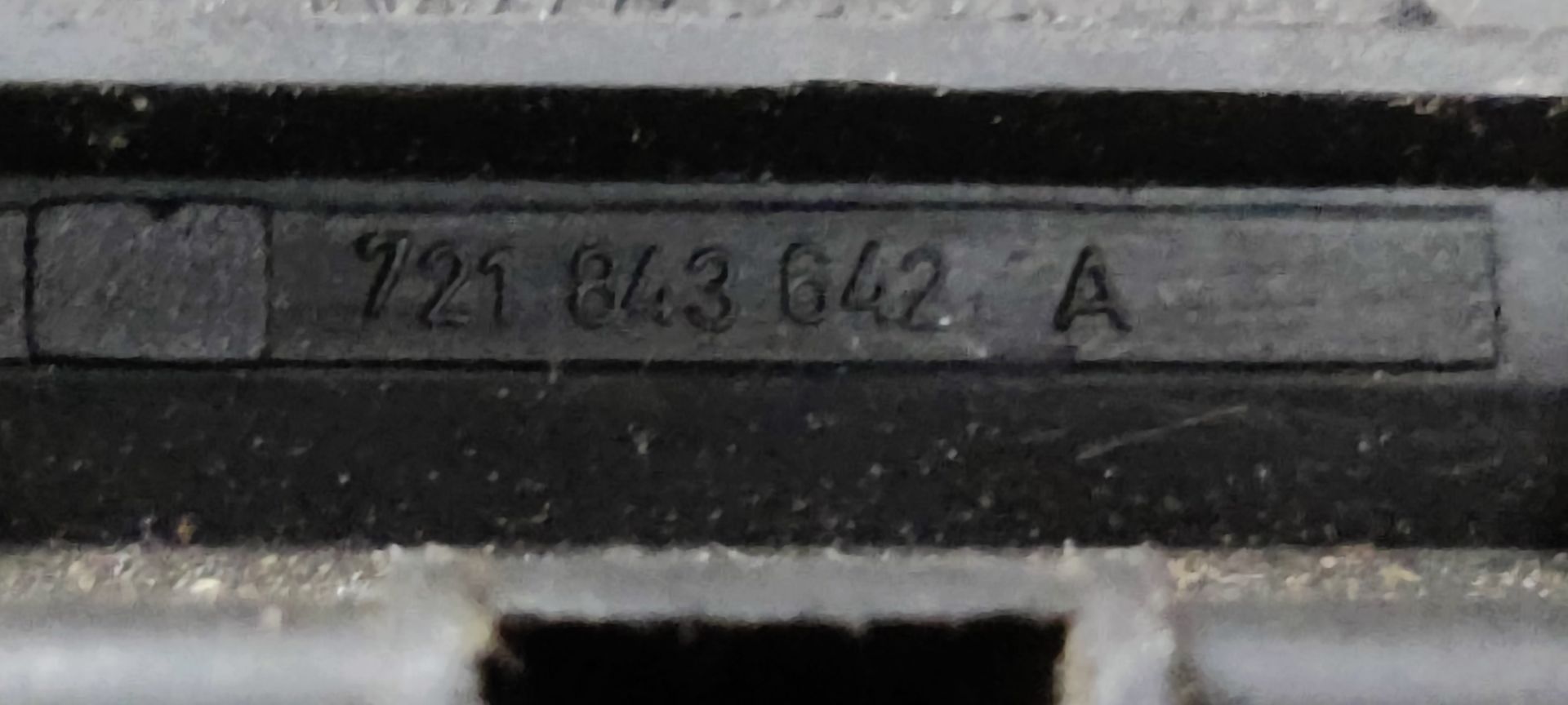 Een zwarte autodeurhendel met een metalen verbindingsstang, liggend op een grijze ondergrond.