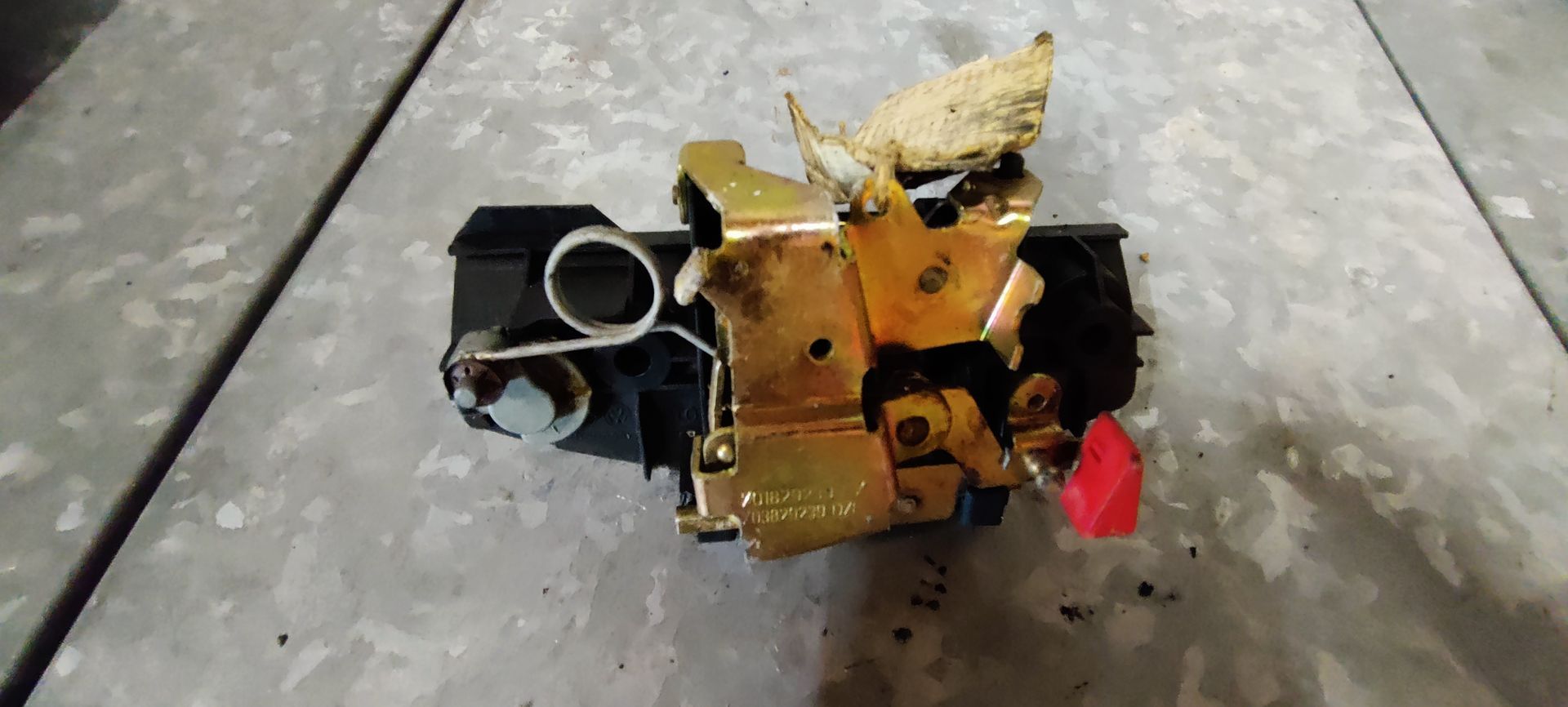 Een zwart autoslot met ingebouwde cilinder voor de kofferbak of achterklep, gezien vanaf de achterkant op een metalen bureau.