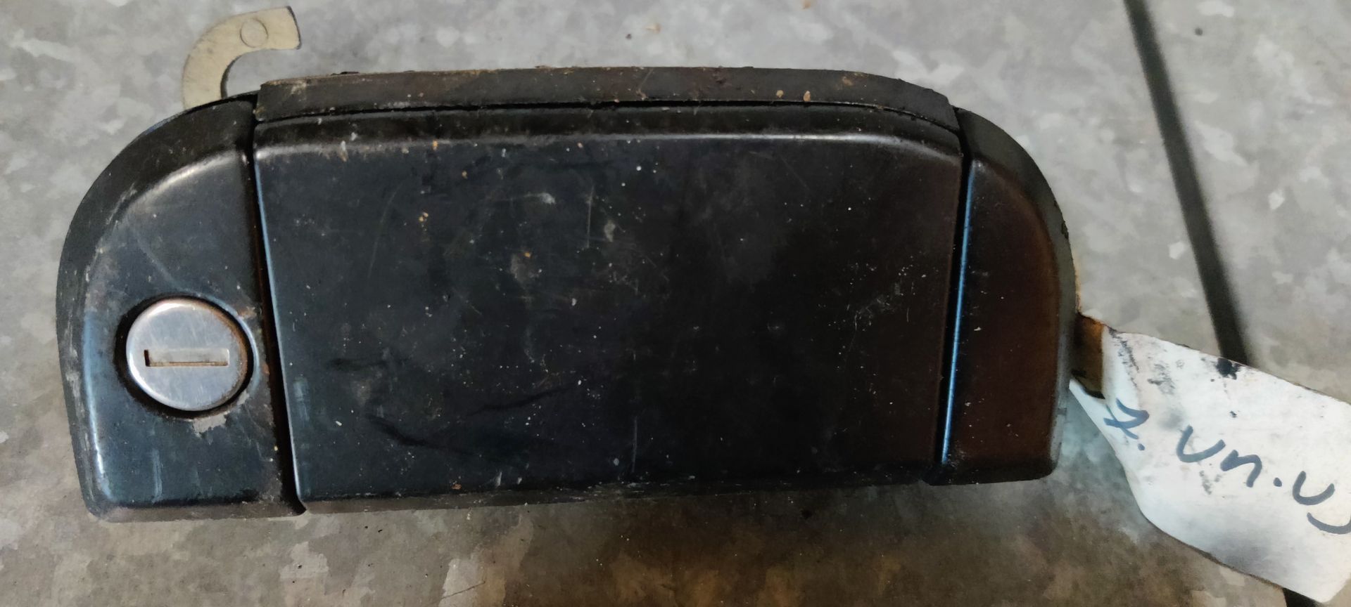 Een zwarte buitendeurhendel voor auto's met geïntegreerd sleutelcilinder, gezien vanaf de voorkant.