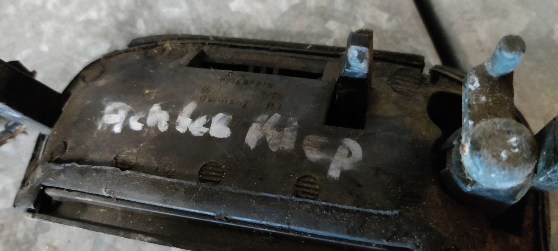 Een zwart, rechthoekig plastic onderdeel van een autohandgreep met handgeschreven witte tekst