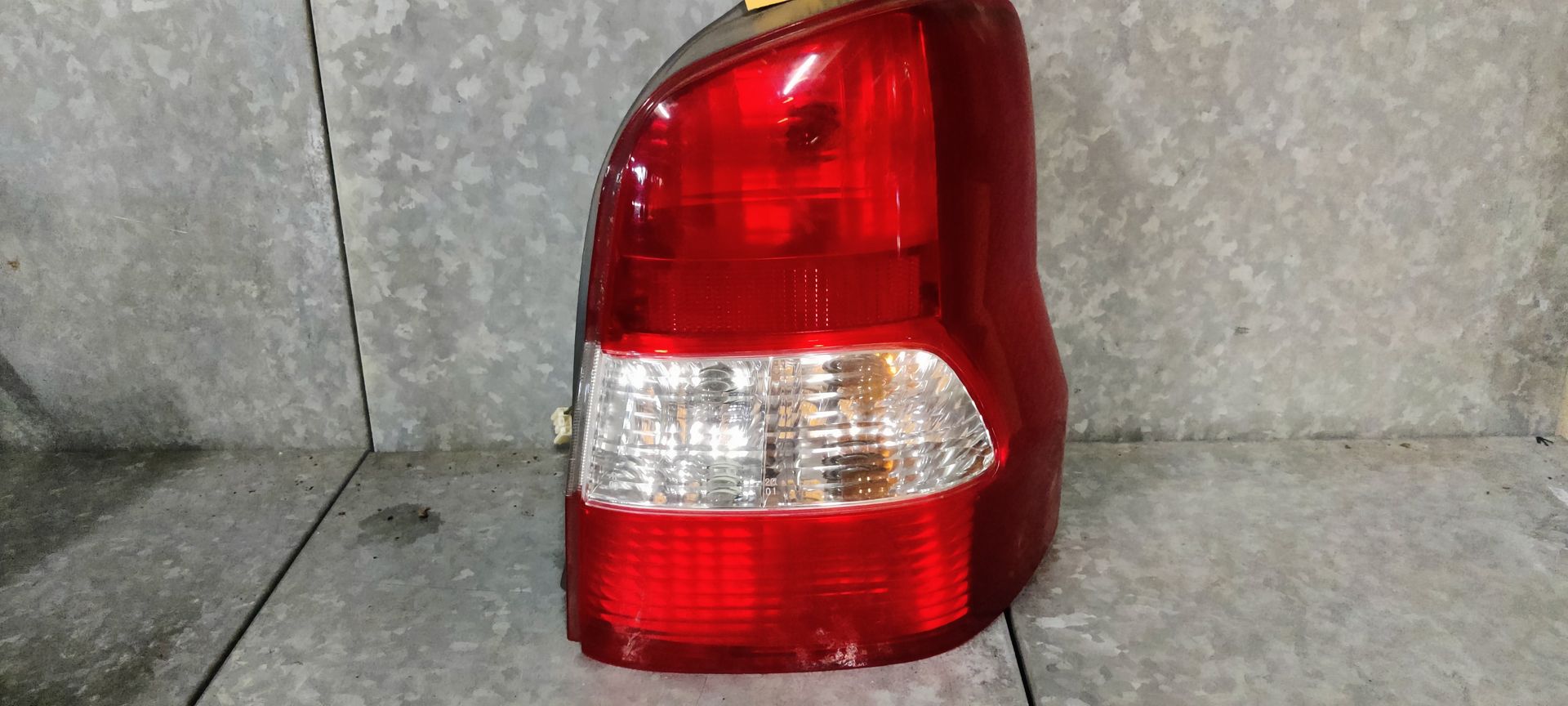 Een rood-witte achterlichtunit van een auto, afgebeeld tegen een grijze achtergrond.