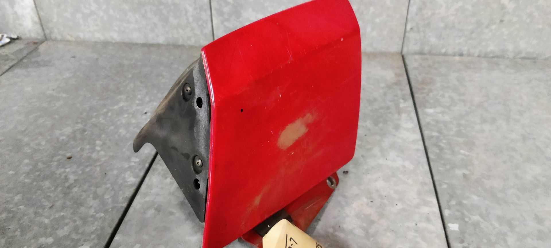 Een rechthoekige, verweerde autokoplampunit met een verchroomde glazen lens in een donkergrijze kunststof behuizing.
