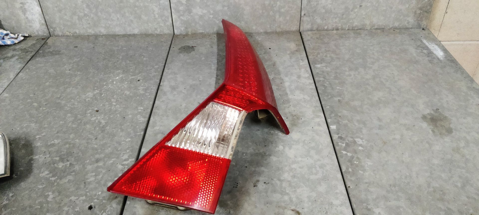 Een rode en transparante achterlichtunit van een auto ligt op een grijze betonnen vloer.