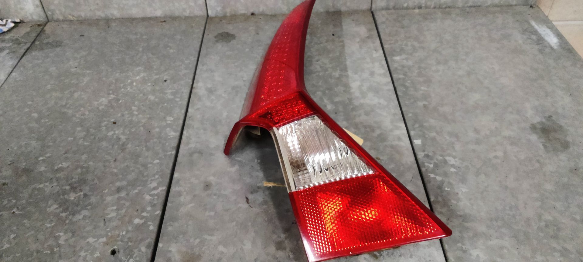 Een schuin geplaatste, rode en transparante plastic achterlichtunit voor auto's ligt op een betonnen vloer.