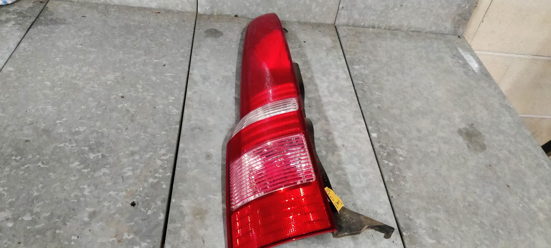 Een rood-witte achterlichtunit van een auto, rustend op een grijze betonnen vloer.