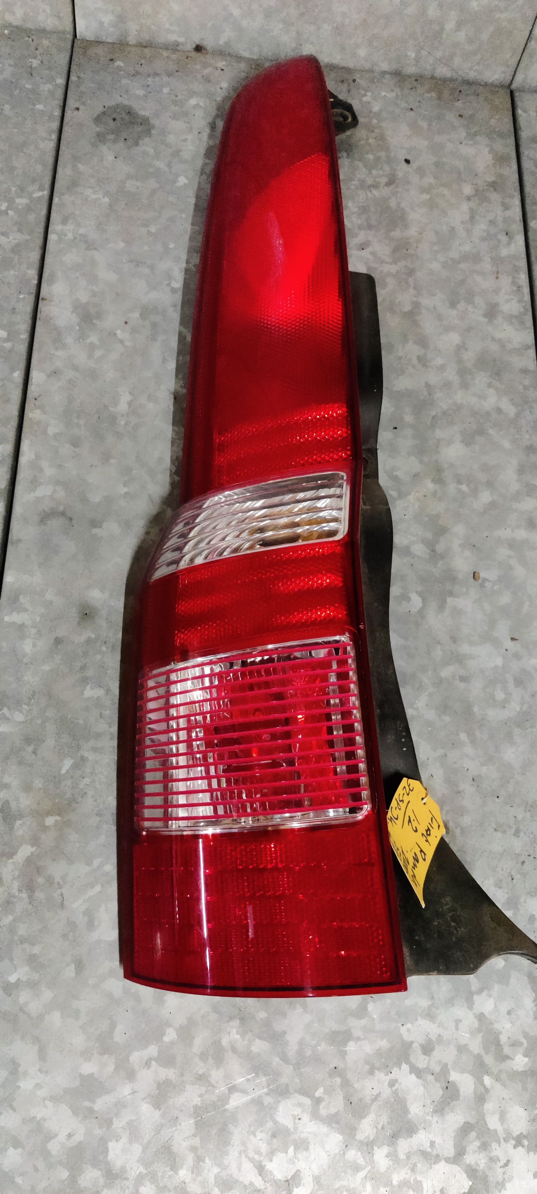 Een rood-witte achterlichtunit van een auto, rustend op een grijze betonnen vloer.