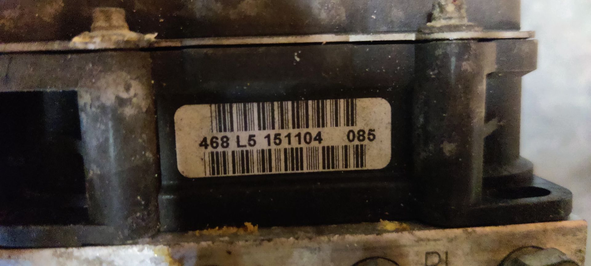 Een metalen motorregelunit voor auto's met een zwarte montagebeugel op een grijze betonnen ondergrond.