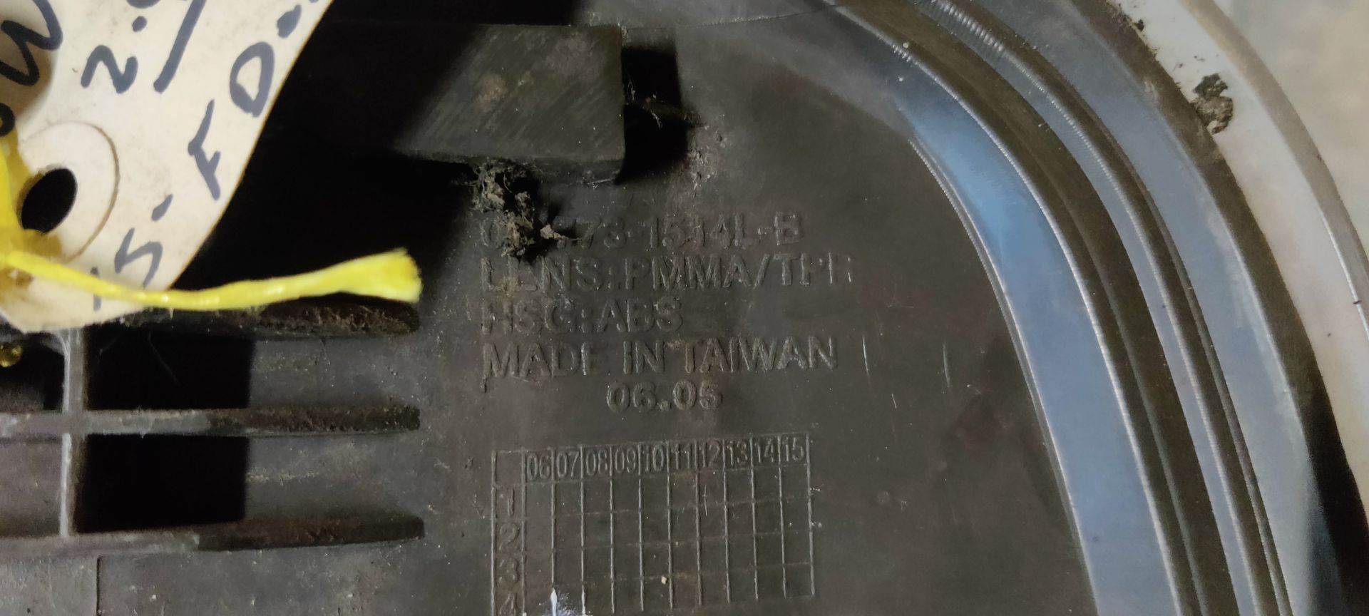 Een enkele autokoplampunit met een zwarte rand en een transparante reflectorlens, rustend op een grijze betonnen vloer.