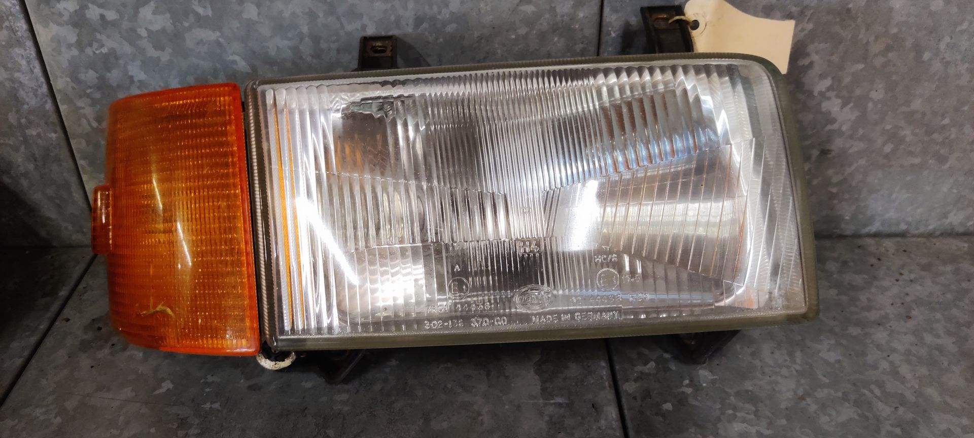 Een rechthoekige autokoplampunit met een geïntegreerd amberkleurig knipperlichtlens op een grijs oppervlak.