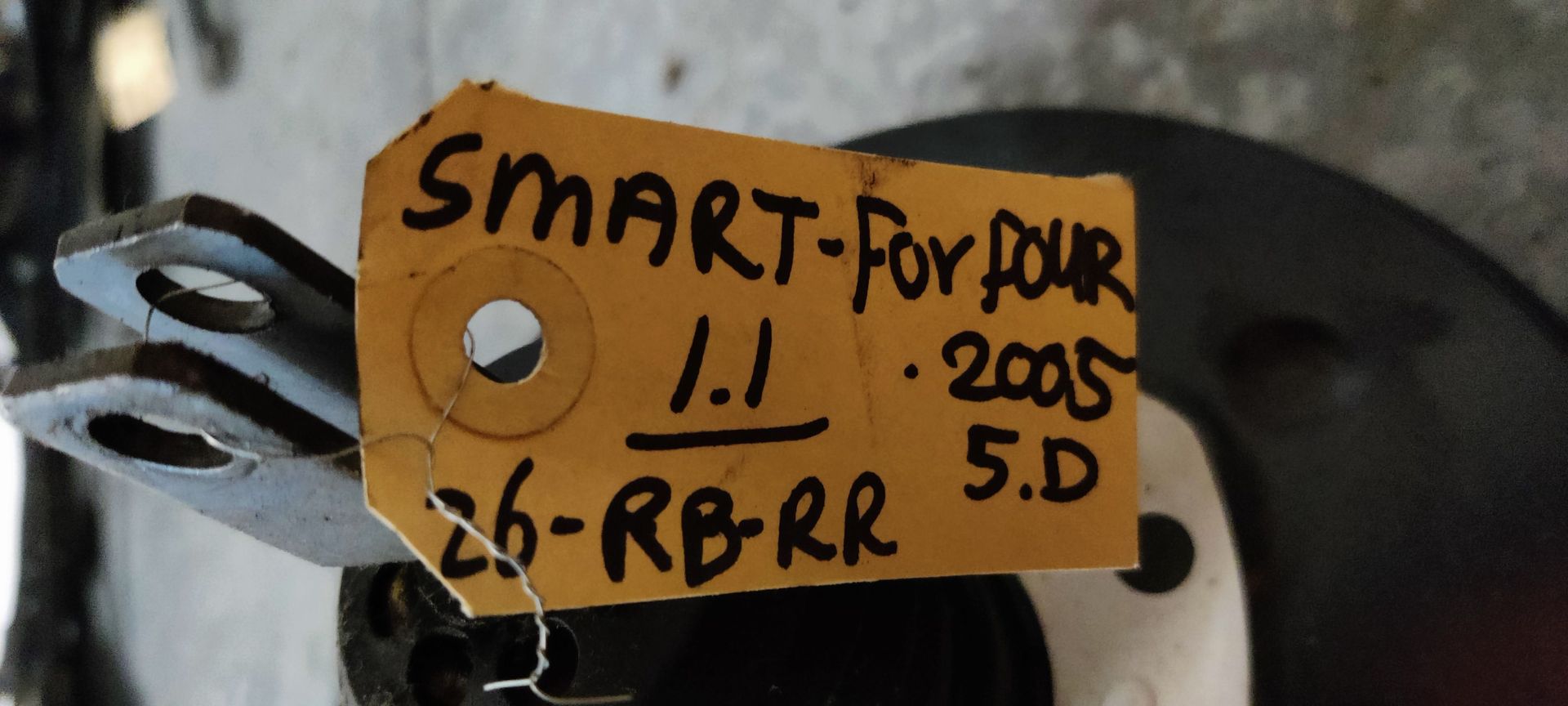Een zwarte Mitsubishi-rembekrachtiger met een wit identificatielabel, van achteren gezien op een metalen oppervlak.