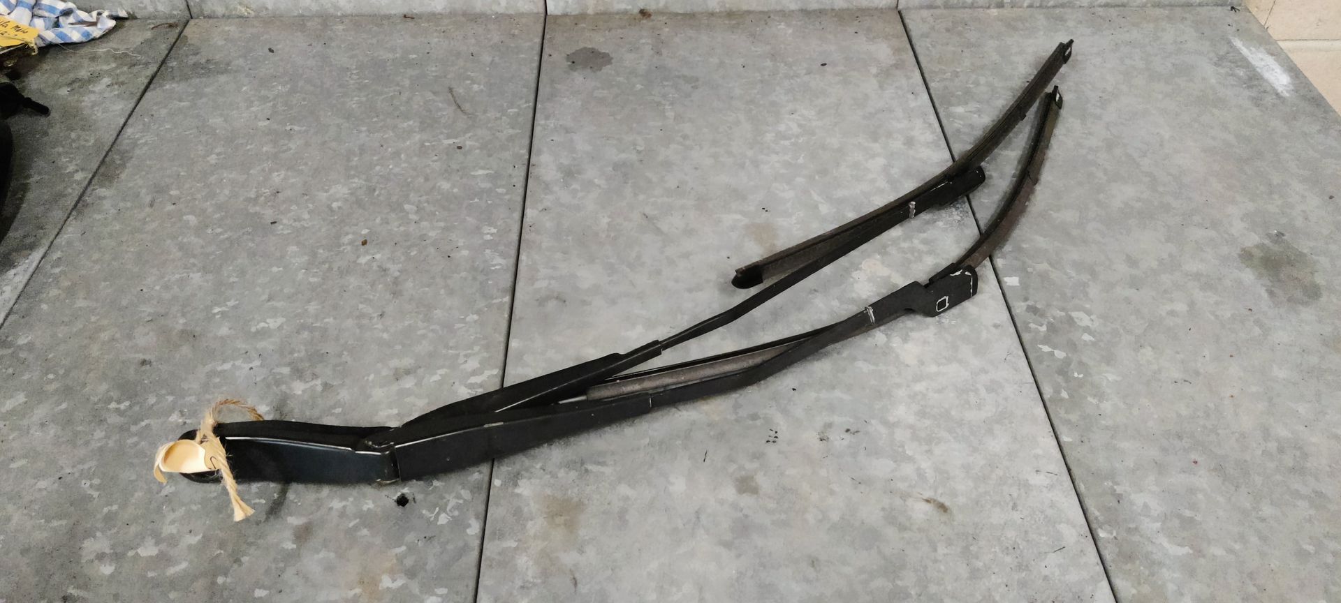 Twee zwarte metalen ruitenwisserarmen liggen op een grijze betonnen ondergrond.