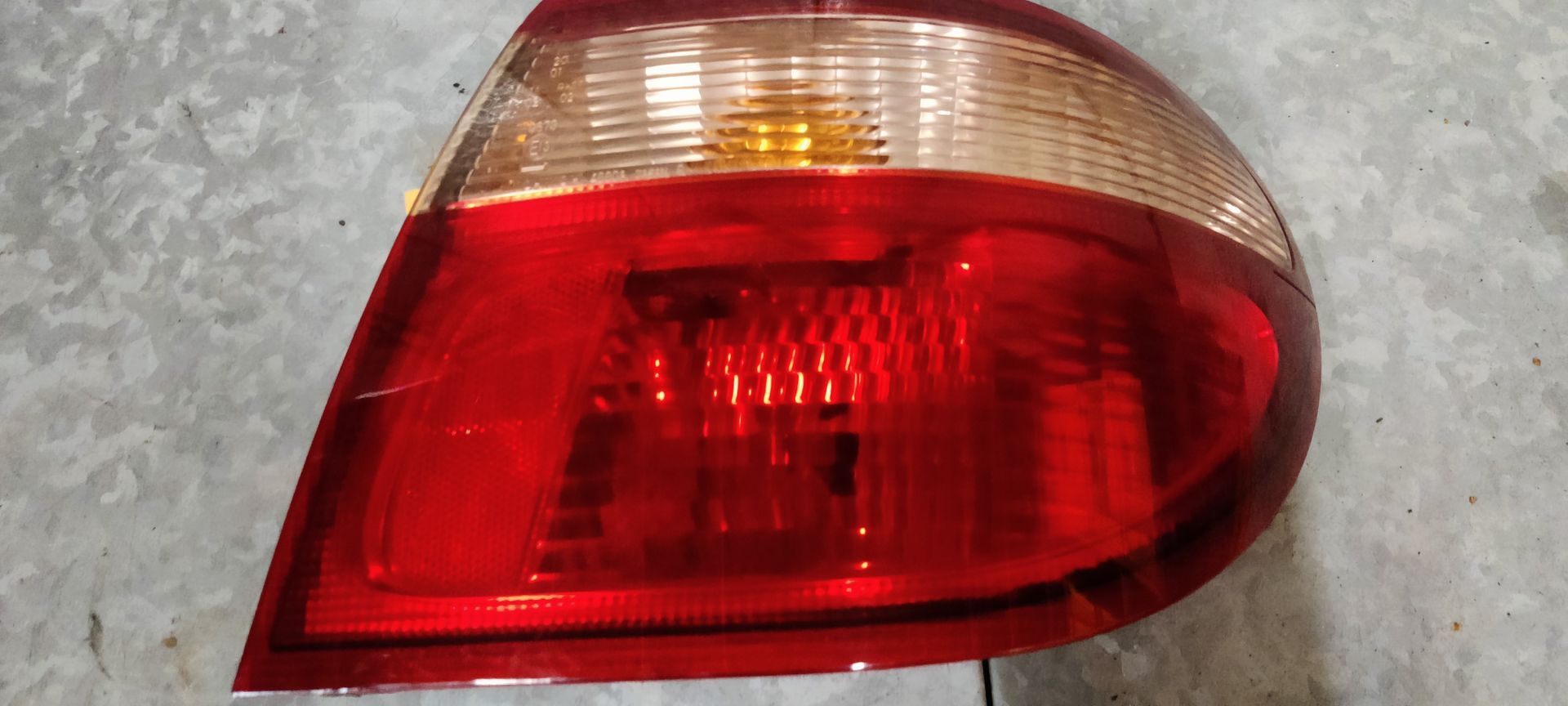 Een rode en transparante plastic achterlichtunit van een voertuig tegen een lichtgrijze achtergrond.