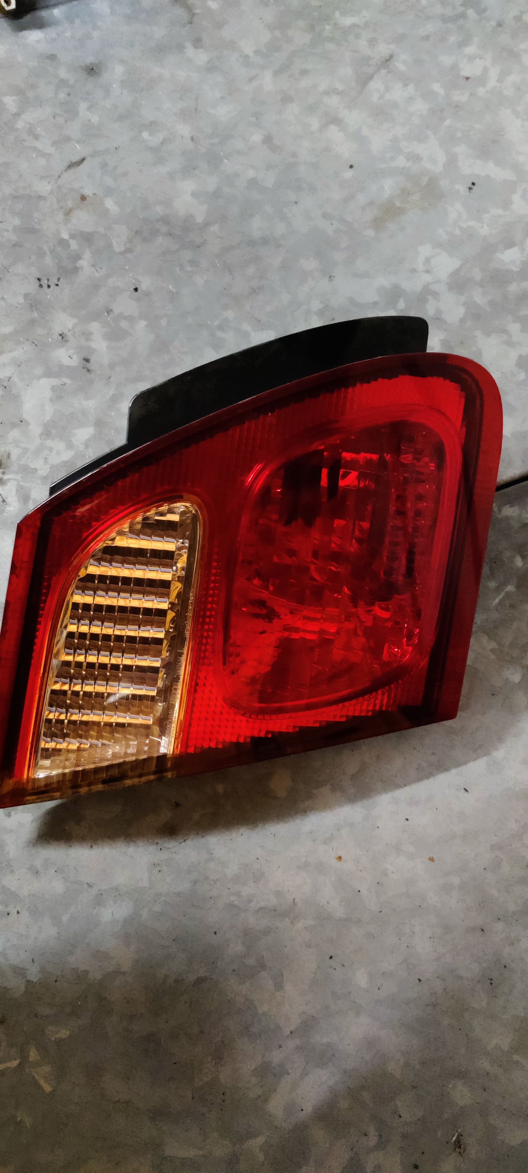Een rode en amberkleurige achterlichtunit van een auto met een zwarte plastic rand, geplaatst op een grijze betonnen vloer.