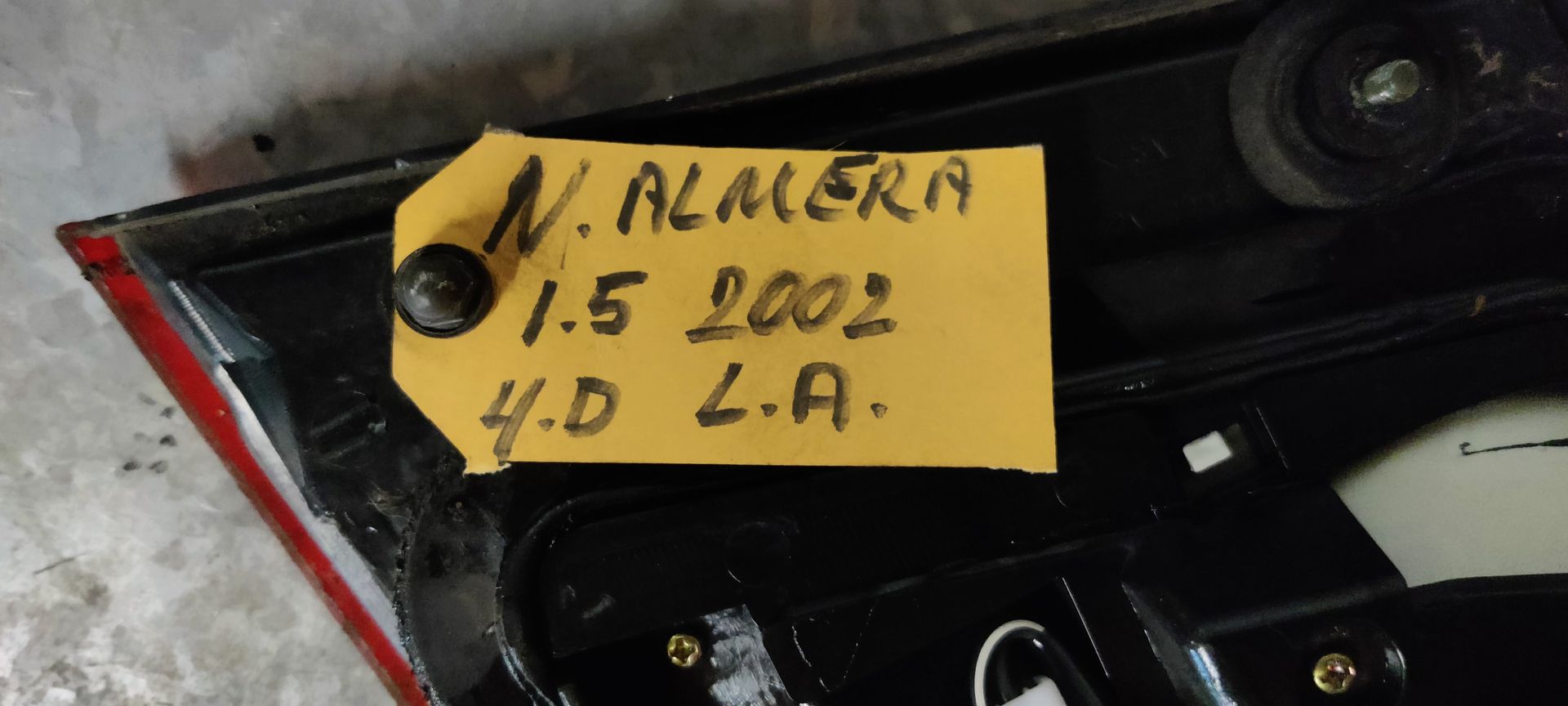 Een rode en amberkleurige achterlichtunit van een auto met een zwarte plastic rand, geplaatst op een grijze betonnen vloer.