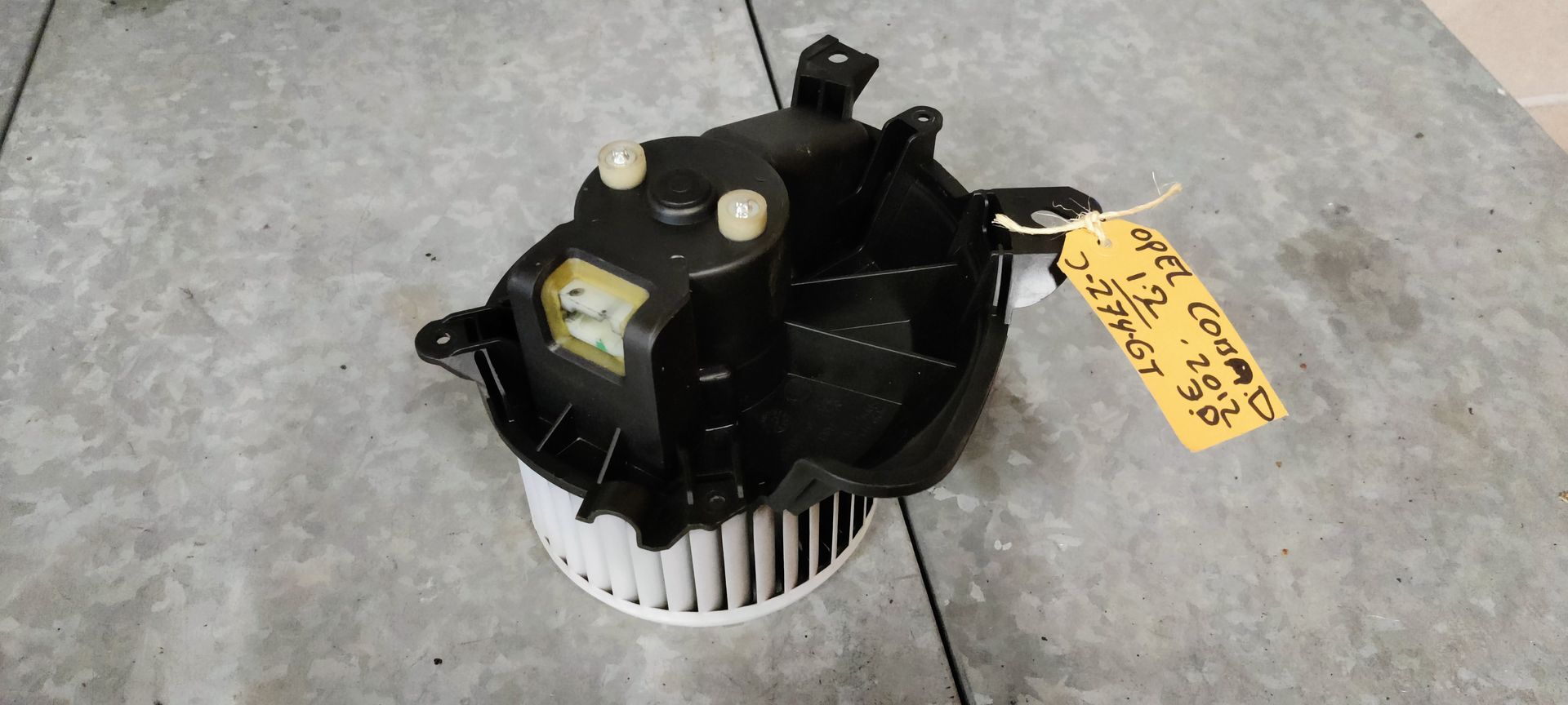 Een autoventilator met een witte centrifugaalventilator en een zwarte behuizing, staand op een grijze vloer.