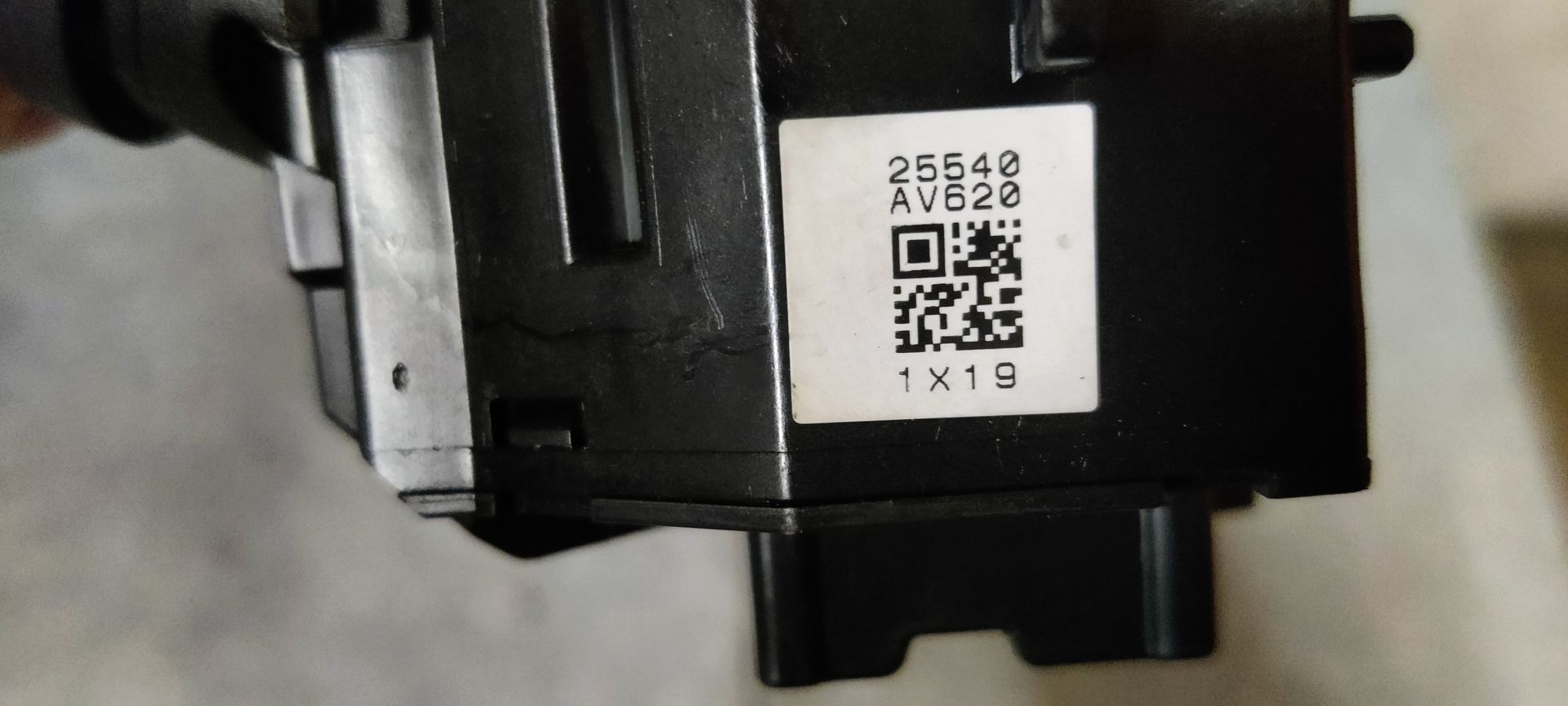 Een zwarte stuurkolomhendel voor richtingaanwijzers en verlichting met witte pictogrammen, rustend op een metalen oppervlak.