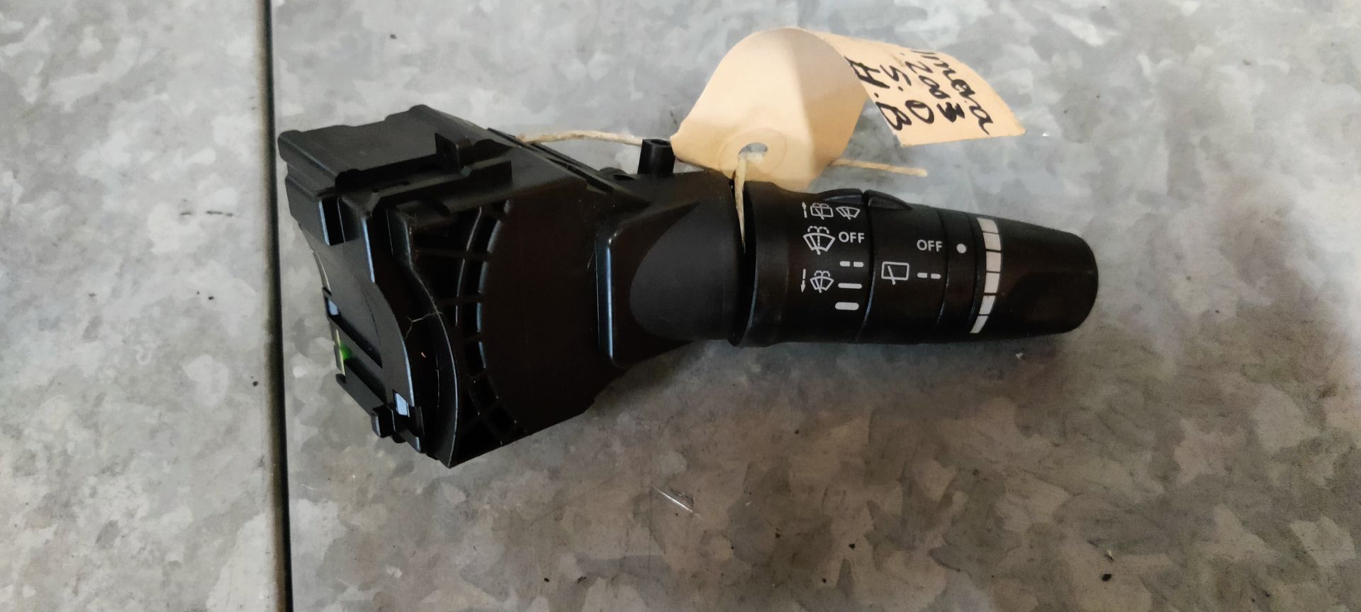 Een zwarte bedieningshendel voor koplampen en richtingaanwijzers met witte pictogrammen, rustend op een metalen oppervlak.