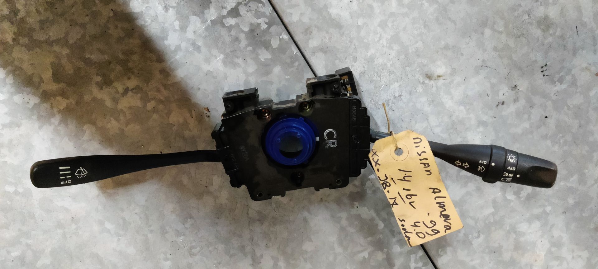 Een zwarte stuurkolomschakelaar voor een Nissan Almera, met een handgeschreven label eraan.